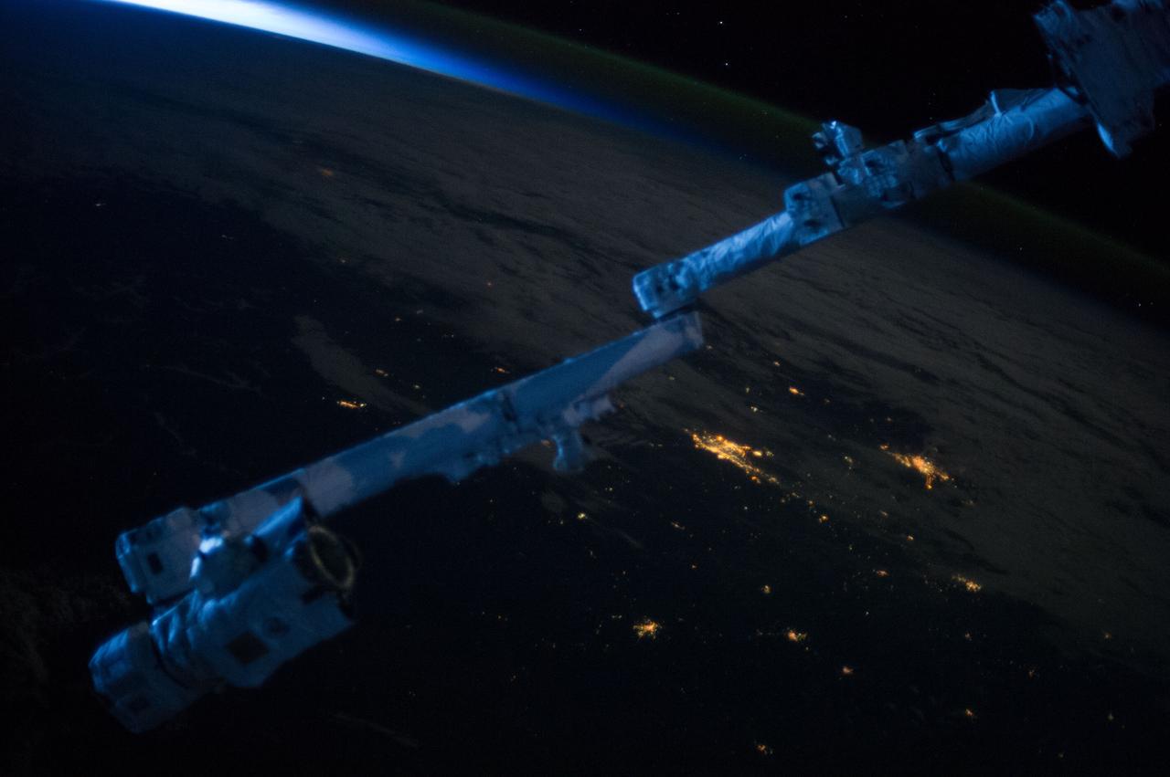 Earth observation taken during night pass by an Expedition 36 crew member on board the International Space Station (ISS). Space Station Remote Manipulator System (SSRMS) arm is visible in the foreground. Per twitter message: Sunrise casts blue on #Canadarm2.