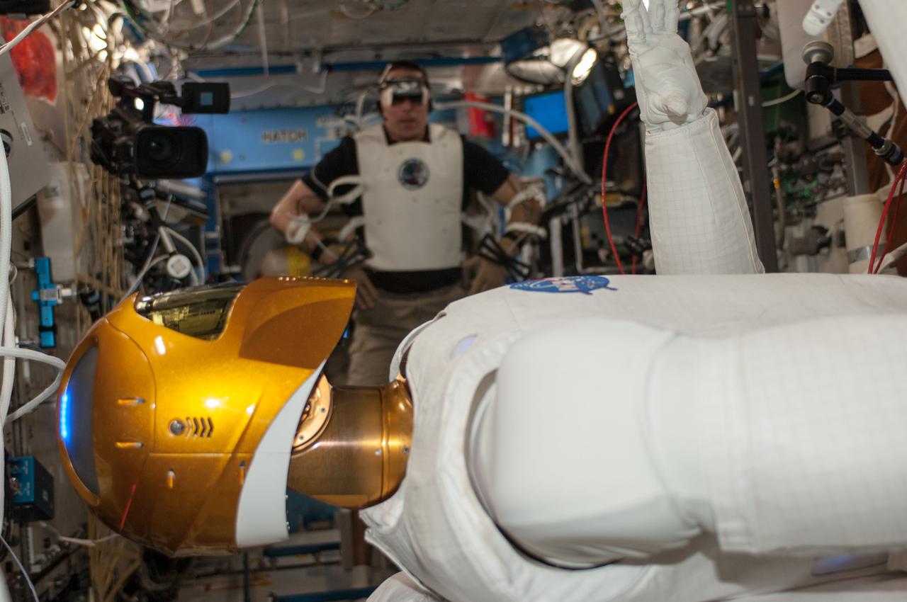 ISS036-E-029110 (6 Aug. 2013) --- In the International Space Station’s Destiny laboratory, NASA astronaut Chris Cassidy, Expedition 36 flight engineer, wears tele-operation gear consisting of a vest, gloves and visor to telerobotically test Robonaut 2’s maneuvers. Cassidy was able to manipulate R2’s head, neck, arms and fingers telerobotically through his own movements as well as through verbal commands.