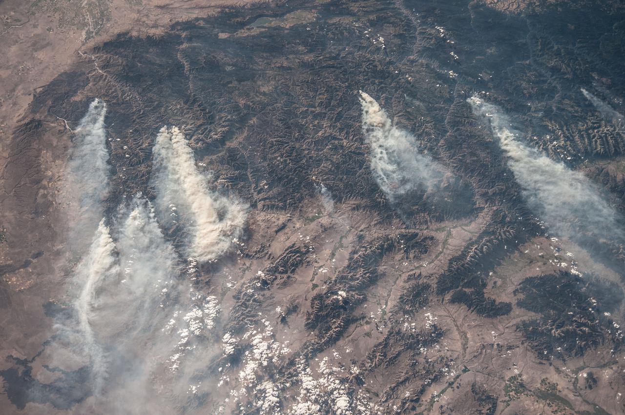 ISS036-E-032853 (18 Aug. 2013) --- Central Idaho wildfires are featured in this image photographed by an Expedition 36 crew member on the International Space Station. Taken with a short lens (50 mm), this west-looking image covers much of forested central Idaho?the dark areas are all wooded mountains. The image highlights part of the largest single wilderness area in the contiguous United States (the Frank Church-River of No Return Wilderness). Within this mountainous region, several fires can be seen producing extensive smoke plumes. Some fires had been named by Aug. 20, 2013, two days after the image was taken. The densest smoke on that day appears to be generated by a combination of the Little Queens and Leggit fires (left, within the Salmon River Mountains). The named fires were mostly set by lightning, and on Aug. 20 totaled 53,000 acres of burned forest south of the Salmon River, and many more if the unnamed fires are included. The Gold Pan fire north of the Salmon River had burned 27,000 acres. For a sense of scale in this oblique view, the Gold Pan fire lies about 125 miles north of the Little Queens fire. This image shows the common pattern of westerly winds transporting smoke in an easterly direction, as seen during the wildfire season of one year ago. Ten days before this image was taken, fires in central Idaho near Boise were aggravated by southerly winds. Some of the fires began to burn in July but were quelled and remain under observation for new flare-ups. Smoke from fires in the south partly obscures the black lava flows of the Craters of the Moon National Monument (lower left). The Beaverhead Mountains mark the eastern boundary of Idaho with Montana.