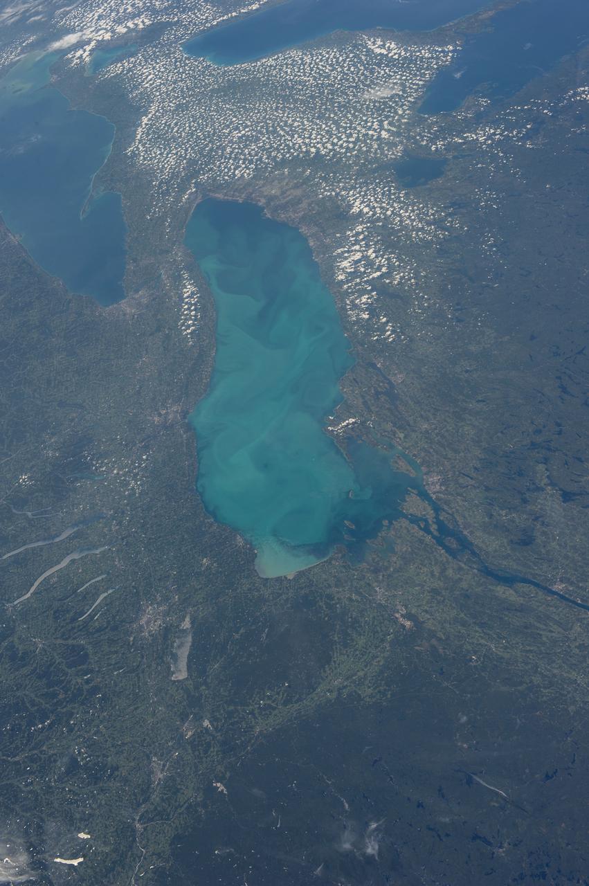 ISS036-E-035635 (24 Aug. 2013) --- Plankton bloom and Lake Ontario are featured in this image photographed by an Expedition 36 crew member on the International Space Station. This photograph highlights a late summer plankton bloom visible throughout much of Lake Ontario (one of the Great Lakes, together with Michigan, Superior, Erie, and Huron). Cyanobacteria, or blue-green algae, can reach such large concentrations that they color the water to such an extent that the change is visible from orbit. Harmful algal blooms, or HABs, have been observed in all of the Great Lakes – particularly Lake Erie - and are associated with a variety of causative factors including changes in precipitation; drought; invasive species (quagga, zebra mussels, Asian carp); nutrient loading from runoff and sewage (nitrogen and phosphorus); and warmer average temperatures. In addition to reduced water quality and human health concerns, algal blooms can also lead to hypoxia (reduction of oxygen in the bottom waters) that kills large numbers of fish and other aquatic life. Lake Ontario, like the other Great Lakes Erie, Huron, and Superior is roughly divided between the USA and Canada. The USA side of Lake Ontario has its shoreline along the state of New York, while its Canadian shoreline lies within the province of Ontario. The city of Kingston, Ontario, is visible near the Saint Lawrence River outflow from the lake. Several other landscape features of New York State are visible in the image, including the Finger Lakes region to the west of Syracuse, NY (upper left). To the northeast of Syracuse, the dark wooded slopes of the Adirondack Mountains are visible at lower right. Patchy white cloud cover obscures much of the land surface to the west of Lake Ontario.