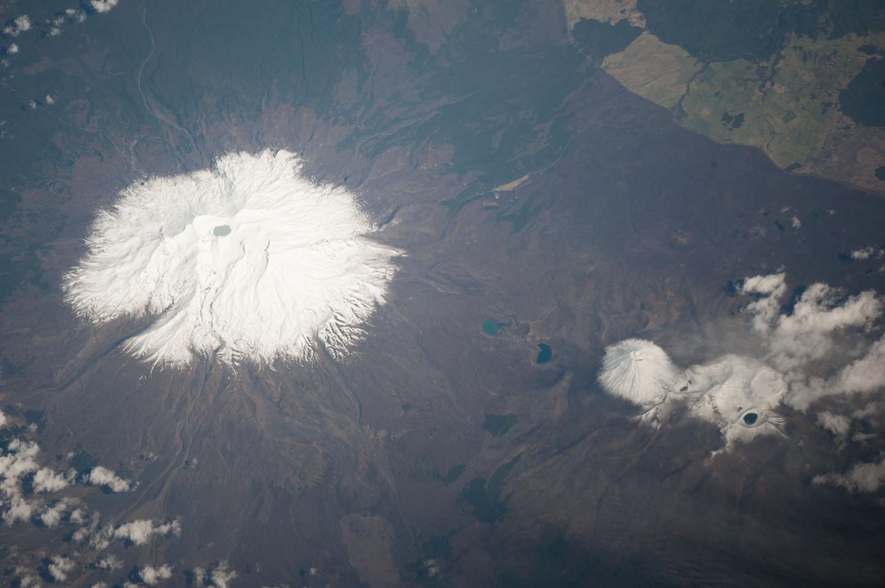 ISS037-E-005089 (30 Sept. 2013) --- Ruapehu volcano and Tongariro volcanic complex in New Zealand are featured in this image photographed by an Expedition 37 crew member on the International Space Station. Mount Ruapehu is one of several volcanic centers on the North Island of New Zealand, but is the largest and historically most active. The 2,797-meter elevation volcano is also the highest mountain on North Island and is covered with snow on its upper slopes. Scientists believe while there are three summit craters that have been active during the last 10,000 years, South Crater is the only historically active one. This vent is currently filled with a lake (Crater Lake), visible at left; eruptions from the vent, mixed with water from the lake can lead to the formation of lahars – destructive gravity flows of mixed fluid and volcanic debris that form a hazard to ski areas on the upper slopes and lower river valleys. The most recent significant eruption of Ruapehu took place in 2007 and formed both an eruption plume and lahars. The volcano is surrounded by a 100-cubic-kilometer ring plain of volcaniclastic debris that appears dark grey in the image, whereas vegetated areas appear light to dark green. Located to the northeast of the Ruapehu volcanic structure, the Tongariro volcanic complex (lower right) is currently in an active eruptive phase – the previous eruptive phase ended in 1897. Explosive eruptions occurred in 2012, which have been followed by steam and gas plumes observed almost daily. According to scientists, the volcanic complex contains multiple cones constructed over the past 275,000 years. The most prominent of these, Mount Ngauruhoe, last erupted in 1975. Like Ruapehu, the upper slopes of both Ngauruhoe and the upper peaks of Tongariro are snow-covered. Scattered cloud cover is also visible near Tongariro at lower right.
