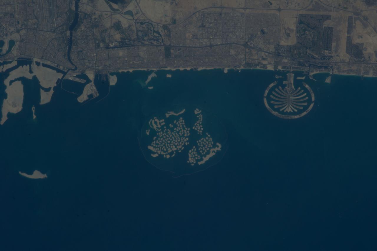 ISS037-E-011470 (14 Oct. 2013) --- Man-made archipelagos near Dubai, United Arab Emirates, are featured in this image photographed by an Expedition 37 crew member on the International Space Station, flying at approximately 220 miles above Earth. The municipality of Dubai is the largest city of the Persian Gulf emirate of the same name, and has built a global reputation for large-scale developments and architectural works. Among the most visible of these developments -- particularly from the perspective of astronauts onboard the space station -- are three man-made archipelagos. The two Palm Islands -- Palm Jumeirah (right) and Palm Jebel Ali (out of frame further to the right) -- appear as stylized palm trees when viewed from above. The World Islands (center frame) evoke a rough map of the world from an air- or space-borne perspective. The Palm Jumeirah project began in 2001 and required more than 50 million cubic meters of dredged sand to raise the islands above the Persian Gulf sea level. Construction of the Palm Jumeirah islands was completed in 2006; for several years now they have been developed for residential and commercial housing and infrastructure. Creation of the World Islands was begun in 2003 and completed in 2008, using 320 million cubic meters of sand and 37 million tons of rock for the surrounding 27 kilometer-long protective breakwater.