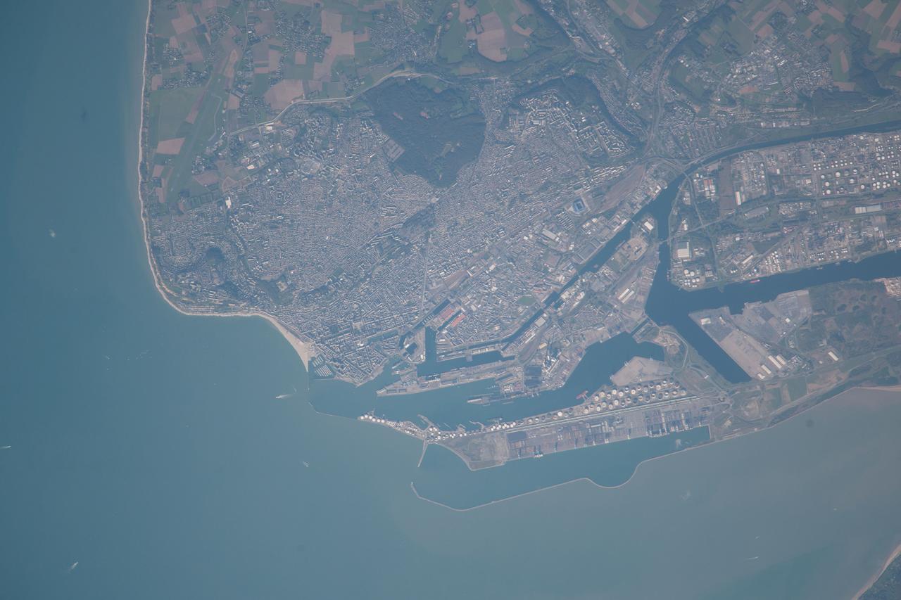 ISS037-E-021618 (26 Oct. 2013) --- Le Havre, France is featured in this image photographed by an Expedition 37 crew member on the International Space Station. The port city of Le Havre, France is located at the confluence of the Seine River and the English Channel along the northern coastline of the country (Upper Normandy region). Le Havre is the largest container port in France, and the second largest in terms of total traffic after Marseille. The extensive port facilities, visible at center, include numerous docks (large cargo ships are clearly visible in this detailed photograph), storage tanks for petro- and other chemicals, and large industrial and warehouse facilities with white rooftops. The port also serves seagoing pleasure cruise vessels. The southern edge of the port facility along the Seine includes a seawall-enclosed ship turning area (lower center). The Montgeon Forest, visible as a large green region at upper center, includes 200 hectares of woodland and 30 hectares of meadows and lawns. The urban area of Le Havre, to the north of the port facilities, was largely destroyed during World War II. After the war, the city was rebuilt following the vision of architect Auguste Perret. Perret favored the use of reinforced and precast concrete in building structures, and much of the city built between 1945 and 1964 follows his plan in both form and materials ? leading to the designation of Le Havre as a UNESCO World Heritage Site.
