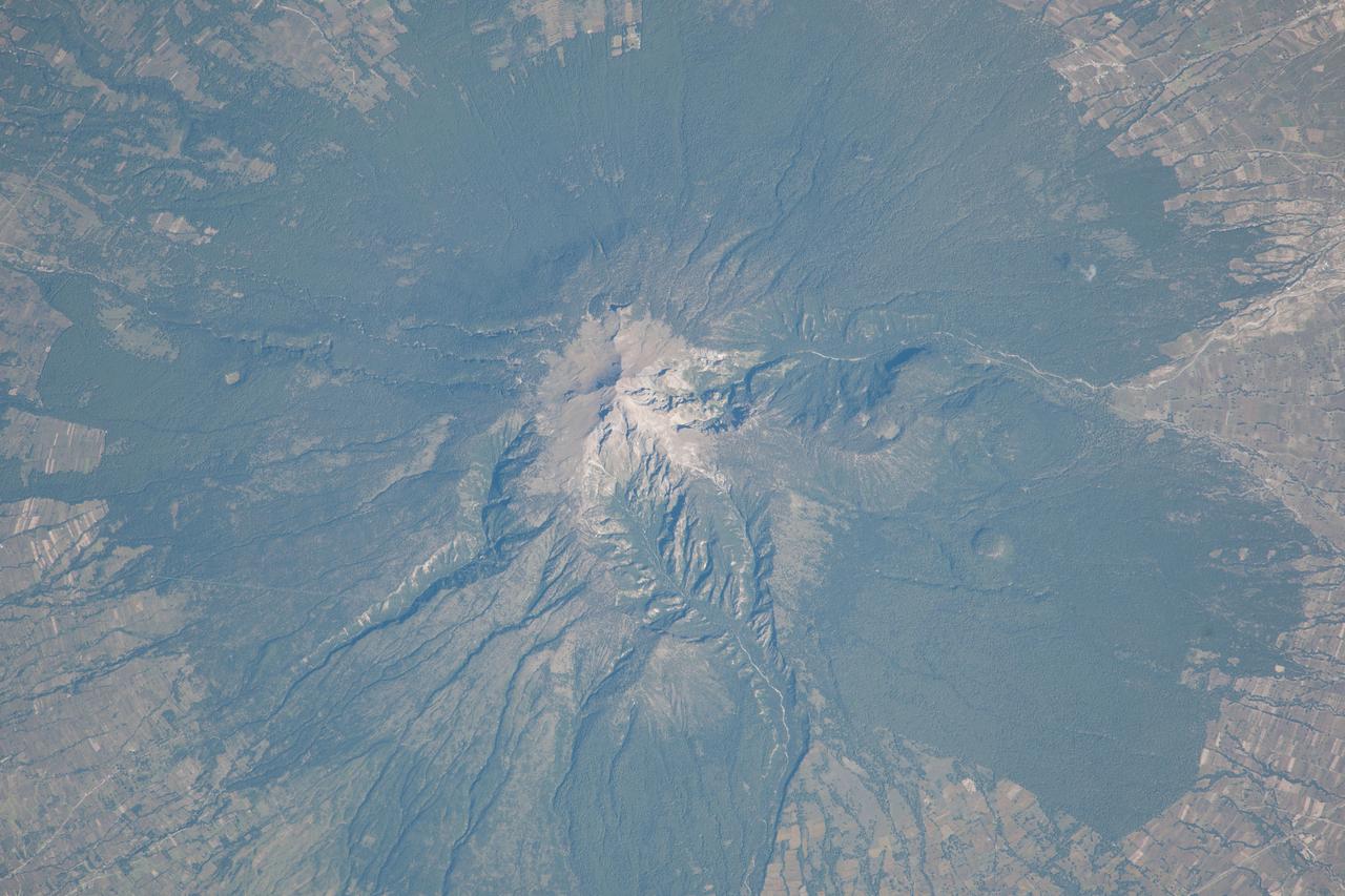 ISS037-E-022473 (29 Oct. 2013) --- La Malinche Volcano, Mexico is featured in this image photo graphed by an Expedition 37 crew member on the International Space Station. Located approximately 30 kilometers to the northeast of the city of Puebla, the summit of Volcan la Malinche rises to an elevation of 4,461 meters above sea level. This detailed photograph highlights the snow-dusted summit, and the deep canyons that cut into the flanks of this eroded stratovolcano. La Malinche has not been historically active, but radiometric dating of volcanic rocks and deposits associated with the structure indicate a most recent eruption near the end of the 12th century. NASA scientists cite evidence that lahars, or mudflows, associated with an eruption about 3,100 years ago, affected Pre-Columbian settlements in the nearby Puebla basin. The volcano is enclosed within La Malinche National Park situated within parts of the states of Puebla and Tlaxcala; extensive green forest cover is visible on the lower flanks of the volcano. Access to the volcano is available through roadways, and it is frequently used as a training peak by climbers prior to attempting higher summits. The rectangular outlines of agricultural fields are visible forming an outer ring around the forested area. While the volcano appears to be quiescent, its relatively recent (in geological terms) eruptive activity, and location within the Trans-Mexican Volcanic Belt– a tectonically active region with several current and historically active volcanoes including Popocatepetl to the west and Pico de Orizaba to the east - suggests that future activity is still possible and could potentially pose a threat to the nearby city of Puebla.