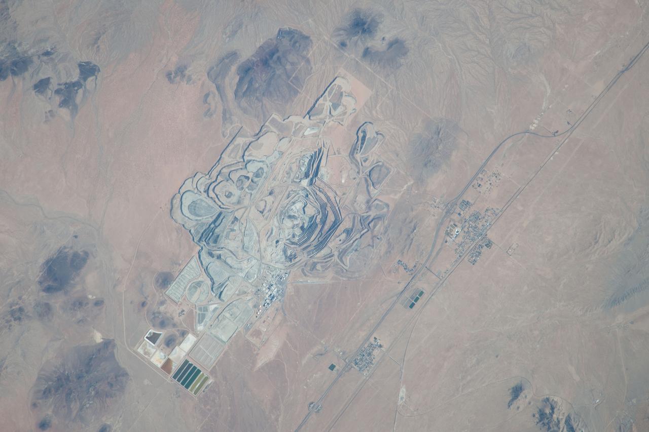 ISS037-E-022990 (30 Oct. 2013) --- This detailed image, photographed by an Expedition 37 crew member on the International Space Station, features the former US Borax mine located to the northwest of Boron, California. The mine, currently owned by the Rio Tinto Group, is the largest open-pit mine in California (covering approximately 54 square kilometers) and is among the largest borate mines in the world. Borates, chemical compounds that include the element boron (B), are important both as providers of an essential plant micronutrient, for metallurgical applications, and as components of specialized types of glass, anticorrosive coatings, fire retardants, and detergents (among other uses). Borate minerals such as borax, kernite, and ulexite are found in deposits at the Rio Tinto borax mine. The geologic setting is a structural, nonmarine basin ? a permanent shallow lake ? fed by thermal springs rich in sodium and boron that existed approximately 16 million years ago, according to scientists. The first mining claim in the area was filed in 1913, following discovery of boron-bearing nodules during well drilling. Much of the mine workings were underground until 1957, when US Borax changed to open-pit mining. The open pit is clearly visible at center; concentric benches along the pit wall are accentuated by shadows and mark successive levels of material extraction. Mine tailings are visible as stacked terraces along the northern boundary of the mine. Ore processing facilities occupy a relatively small percentage of the mine area, and are located directly to the west of the open pit. The Rio Tinto mine is one of the Earth?s richest borate deposits; together with mines in Argentina, they produce almost 40 percent of the world?s supply of industrial borate minerals.