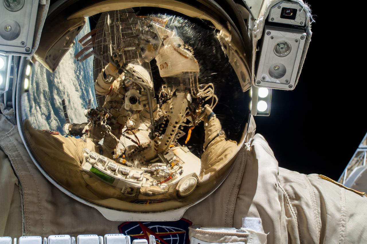 ISS037-E-028076 (9 Nov. 2013) --- Russian cosmonaut Sergey Ryazanskiy, Expedition 37 flight engineer, attired in a Russian Orlan spacesuit, uses a digital still camera to expose a photo of his helmet visor during a session of extravehicular activity (EVA) as work continues on the International Space Station. Also visible in the reflections in the visor are Russian cosmonaut Oleg Kotov, flight engineer, and various components of the space station and a blue and white portion of Earth. During the five-hour, 50-minute spacewalk, Kotov and Ryazanskiy continued the setup of a combination EVA workstation and biaxial pointing platform that was installed during an Expedition 36 spacewalk on Aug. 22.