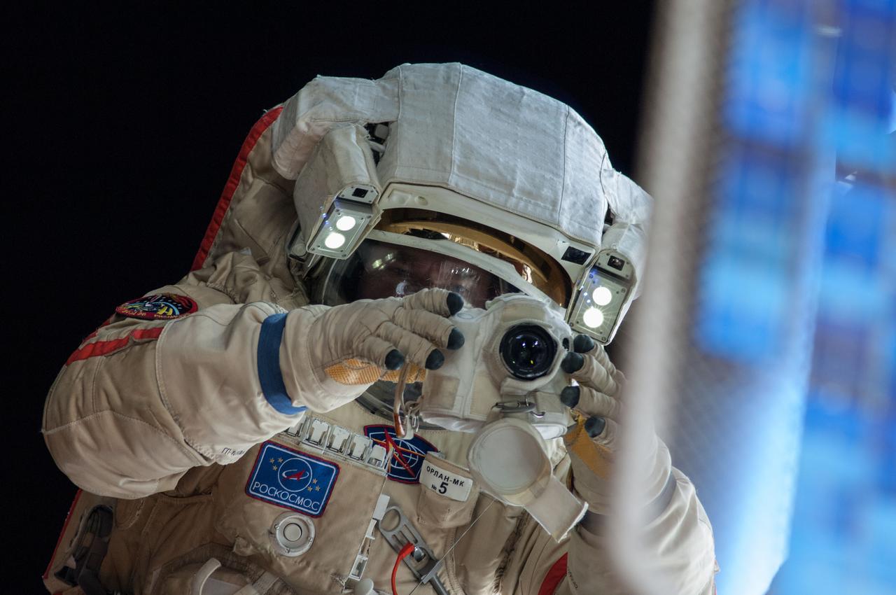 ISS037-E-028569 (9 Nov. 2013) --- Russian cosmonaut Oleg Kotov, Expedition 37 flight engineer, attired in a Russian Orlan spacesuit, uses a still camera during a session of extravehicular activity (EVA) in support of assembly and maintenance on the International Space Station. During the five-hour, 50-minute spacewalk, Kotov and Russian cosmonaut Sergey Ryazanskiy (out of frame) continued the setup of a combination EVA workstation and biaxial pointing platform that was installed during an Expedition 36 spacewalk on Aug. 22.