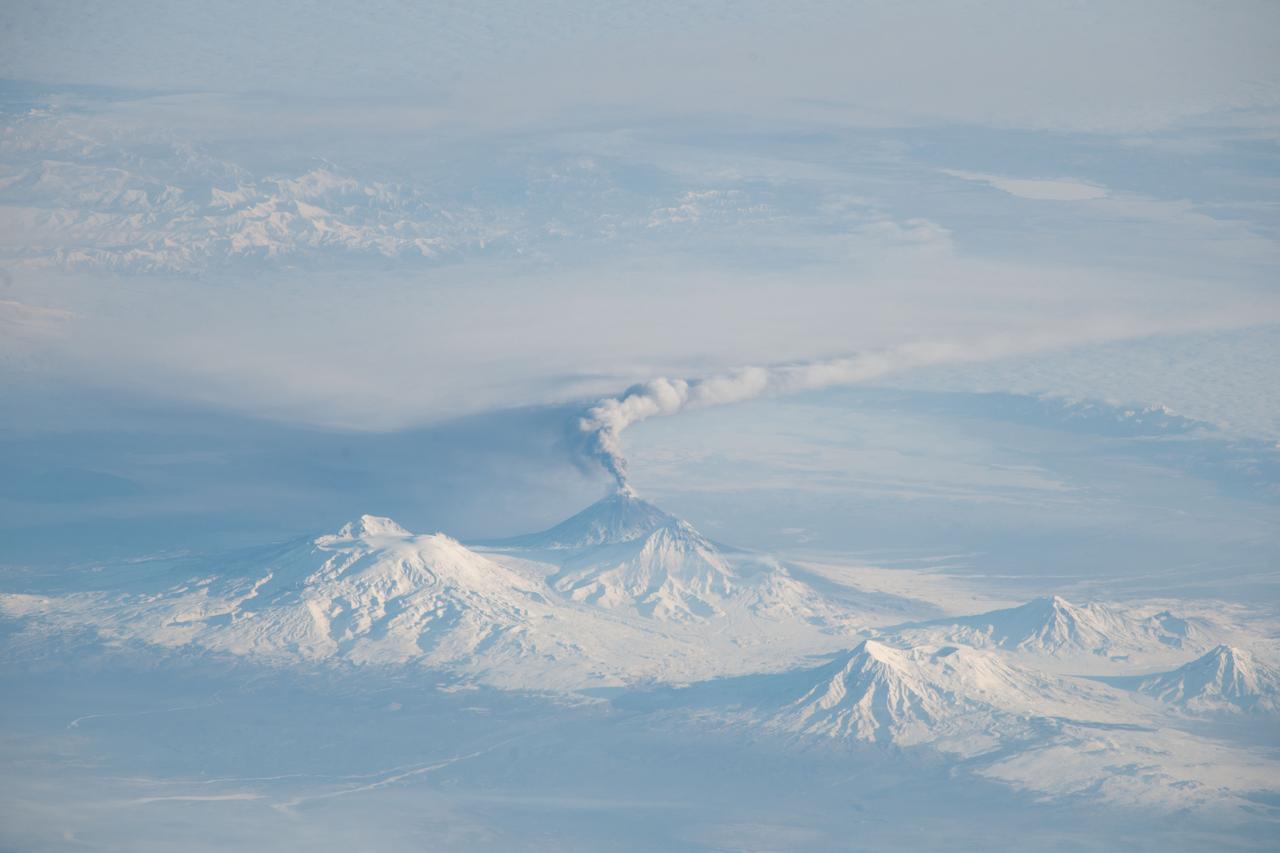 ISS038-E-005515 (16 Nov. 2013) --- Activity at Kliuchevskoi Volcano on Kamchatka Peninsula in the Russian Federation is featured in this image photographed by an Expedition 38 crew member on the International Space Station. When viewing conditions are favorable, crew members onboard the space station can take unusual and striking images of Earth. This photograph provides a view of an eruption plume emanating from Kliuchevskoi Volcano, one of the many active volcanoes on the Kamchatka Peninsula. Nadir views – looking “straight down”—that are typical of orbital satellite imagery tend to flatten the appearance of the landscape by reducing the sense of three dimensions of the topography. In contrast, this image was taken from the ISS with a very oblique viewing angle that gives a strong sense of three dimensions, which is accentuated by the shadows cast by the volcanic peaks. This resulted in a view similar to what a person might see from a low-altitude airplane. The image was taken when the space station was located over a ground position more than 1,500 kilometers to the southwest. The plume – likely a combination of steam, volcanic gases, and ash – is extended to the east-southeast by prevailing winds; the dark region to the north-northwest of the plume is likely a product of both shadow and ash settling out. Several other volcanoes are visible in the image, including Ushkovsky, Tolbachik, Zimina, and Udina. To the south-southwest of Kliuchevskoi lies Bezymianny Volcano which appears to be emitting a small steam plume (visible at center).