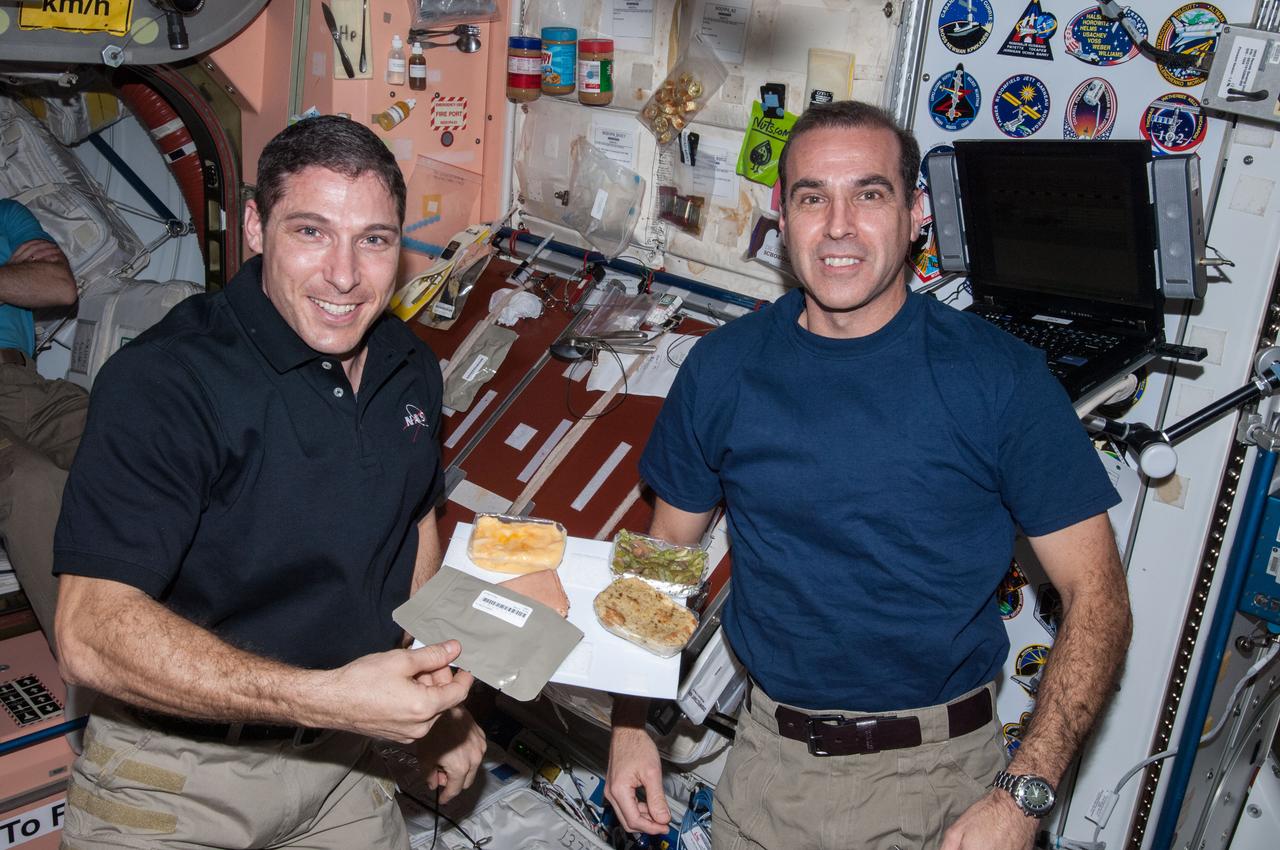 ISS038-E-009306 (28 Nov. 2013) --- NASA astronauts Michael Hopkins (left) and Rick Mastracchio, both Expedition 38 flight engineers, pose for a photo with a Thanksgiving meal in the Unity node of the International Space Station.