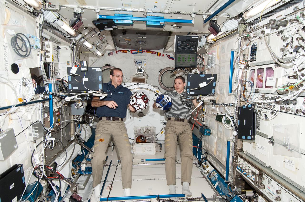 ISS038-E-014008 (9 Dec. 2013) --- In the International Space Station's Kibo laboratory, NASA astronauts Rick Mastracchio (left) and Michael Hopkins, both Expedition 38 flight engineers, conduct a session with a pair of bowling-ball-sized free-flying satellites known as Synchronized Position Hold, Engage, Reorient, Experimental Satellites, or SPHERES.