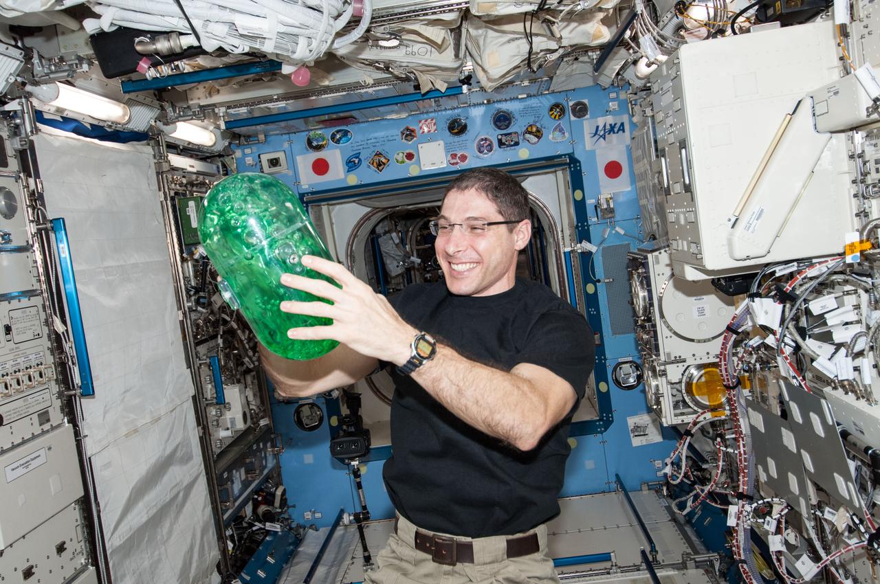 ISS038-E-033884 (22 Jan. 2014) --- In the International Space Station's Kibo laboratory, NASA astronaut Mike Hopkins, Expedition 38 flight engineer, holds a plastic container partially filled with green-colored water which will be used in a new experiment using the soccer-ball-sized, free-flying satellites known as Synchronized Position Hold, Engage, Reorient, Experimental Satellites, or SPHERES, which are already on the station. For the SPHERES-Slosh experiment, two SPHERES robots are attached to opposite ends of a metal frame holding the plastic tank with the green-colored water. The new hardware for the SPHERES-Slosh study was delivered to the station aboard Orbital Sciences' Cygnus cargo craft on Jan. 12.