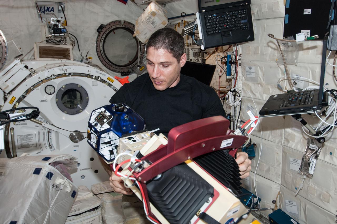 ISS038-E-033890 (22 Jan. 2014) --- In the International Space Station's Kibo laboratory, NASA astronaut Mike Hopkins, Expedition 38 flight engineer, works with a new experiment using the soccer-ball-sized, free-flying satellites known as Synchronized Position Hold, Engage, Reorient, Experimental Satellites, or SPHERES, which are already on the station. For the SPHERES-Slosh experiment, two SPHERES robots are attached to opposite ends of a metal frame holding the plastic tank with the green-colored water. The new hardware for the SPHERES-Slosh study was delivered to the station aboard Orbital Sciences' Cygnus cargo craft on Jan. 12.