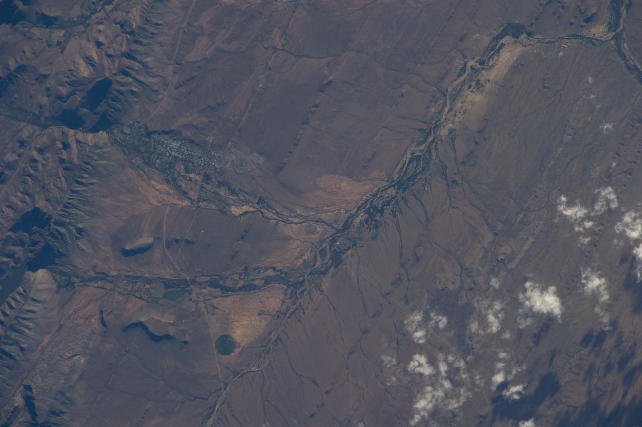ISS038-E-039032 (30 Jan. 2014) --- Prince Albert, South Africa is featured in this image photographed by an Expedition 38 crew member on the International Space Station. Space station crews sometimes take detailed images with an 800mm lens, such as this view of the small town of Prince Albert (population just more than 7,000). The town lies at the foot of the mountains known as the Great Swartberg in southern South Africa, about 220 miles (355 kilometers) east of Cape Town. Prince Albert, named after Queen Victoria's husband, appears as a cluster of whitewashed buildings (left) at the foot of the mountains, larger dwellings nearer the steep mountain front and smaller dwellings further away. Despite its small size, the dry climate and the water supply from gorges immediately upstream (a small reservoir appears extreme left) have made it well-known as a productive point in the Karroo semidesert. Olive groves especially, with other crops, flourish on the valleys floors, surrounded by sheep and ostrich ranches. Founded 250 years ago, this small town retains more than a dozen registered historic buildings in the Victorian and Cape Dutch styles. Based on this and other small Karroo towns as get-aways from South Africa's large, crowded cities, tourism has developed significantly in the last 20 years. Swartberg means Black Mountain in Afrikaans, and winter snow (not visible in this image) along the mountain tops (4,500-6,500 feet; 1,370-1,980 meters, above the town) makes for spectacular scenery. The mountains are part of the ancient Cape Fold Mountain Belt. Gorges through the mountains provide impressive side-on views of tightly folded and broken rock layers associated with the mountain-building episode.