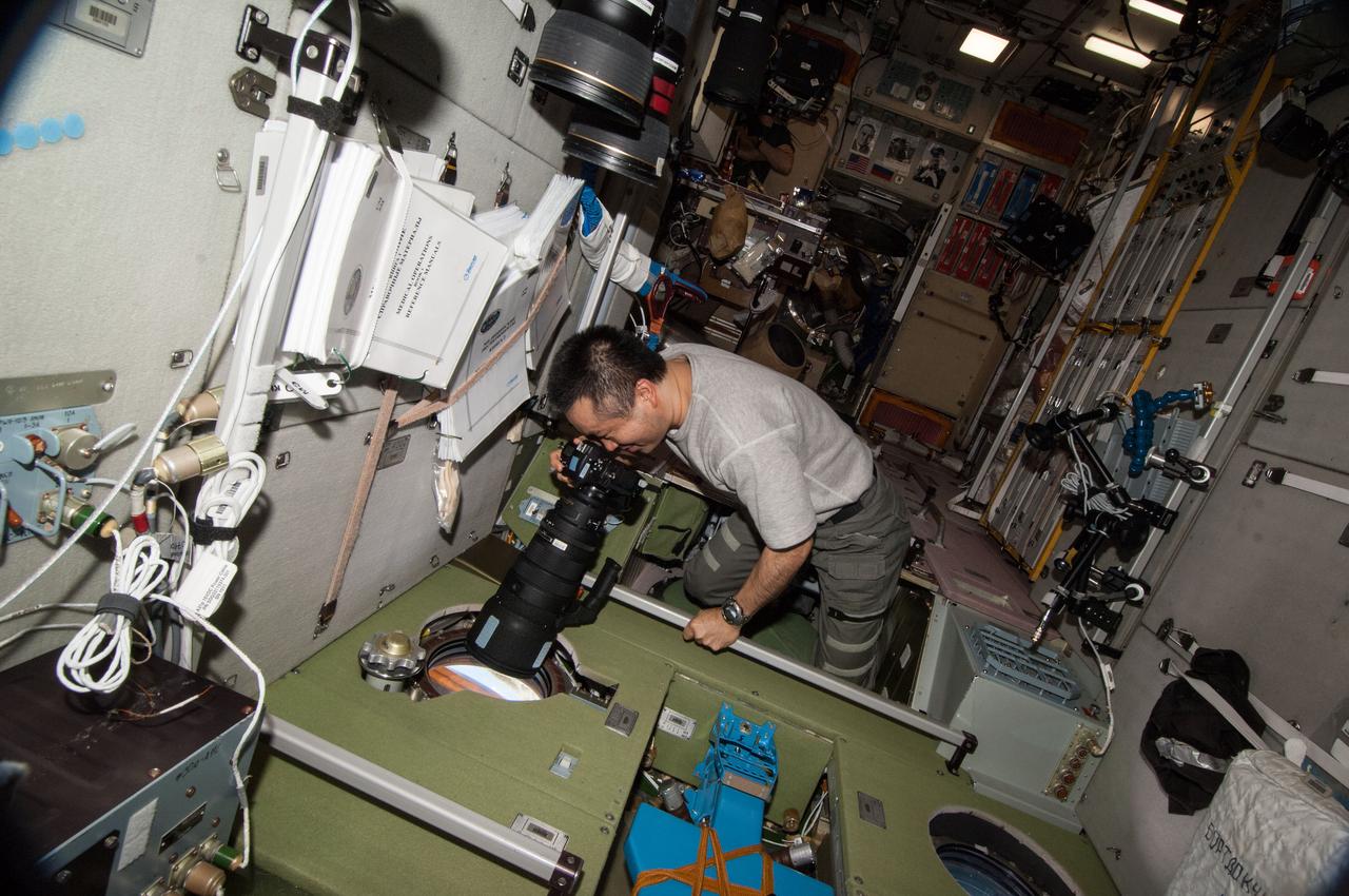 ISS038-E-046882 (13 Feb. 2014) --- Japan Aerospace Exploration Agency astronaut Koichi Wakata, Expedition 38 flight engineer, uses a still camera at a window in the Zvezda Service Module of the International Space Station.