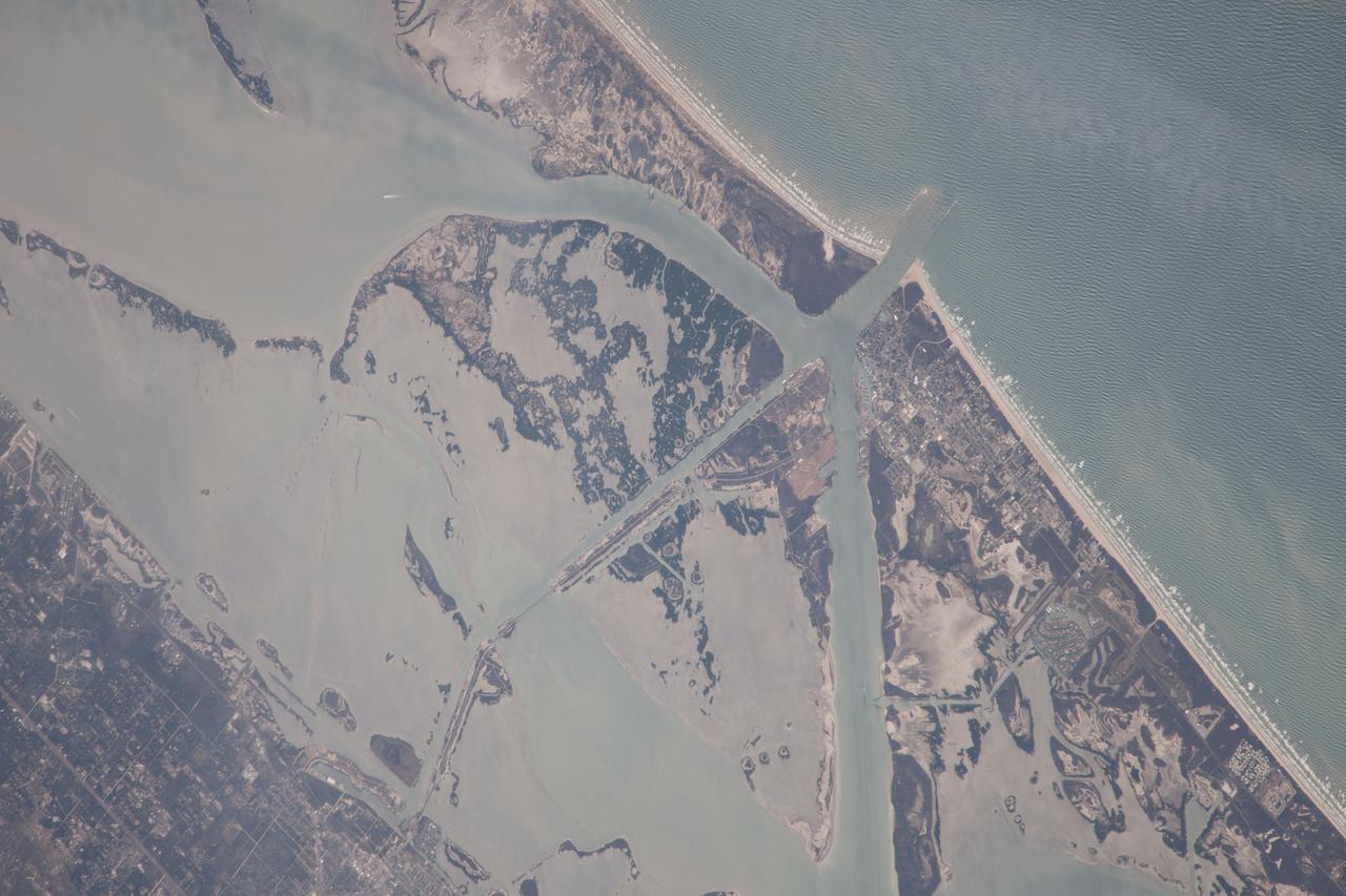 ISS038-E-57806  (21 Feb. 2014) ---  One of the Expedition 38 crew members aboard the International Space Station photographed this image of the Gulf of Mexico's Intracoastal Waterway in southern Texas. Represented in the photo are 18 kilometers (11.2 miles)  of  the overall 4800 kilometers-long (3000 miles) barge channel that lies on the protected inshore of the coastal islands of the southern and eastern USA, including coastal Texas. The small city of Port Aransas lies on a barrier island fully 18 kilometers (11.2 miles) seaward of the mainland and its sister city, Aransas Pass (lower left).  This image shows parts of the waterway that are artificial, as in the straight sector leading into Corpus Christi Bay.  Corpus Christi lies outside the lower margin of the image.  Other sectors of the waterway are natural bays such as Aransas Bay.  Jetties protect the inlet into the Gulf of Mexico (top right). Inlets at many points cut through the barrier islands to give shipping access to the Gulf of Mexico and the Atlantic Ocean.