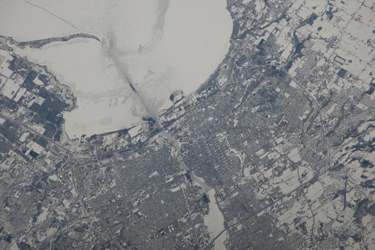 ISS038-E-057979  (22 Feb. 2014)  --- This image, photographed by one of the Expedition 38 crew members aboard the International Space Station, shows the city of Green Bay, Wisconsin at the southern end of icebound Green Bay.  This arm of Lake Michigan is six miles wide as seen in this view.  The heavy snowfalls of the winter of 2014 cover the landscape.  Combined with low sun illumination of a winter day, all surfaces appear as shades of gray.  Fields appear brighter (top right, lower right), the cityscape (lower half of the image) appears as a checkerboard of grays, and forests (top left) appear dark. The center of the city lies on the Fox River, one of the few larger rivers in the United States that flow north.  Open water appears as dark patches at the mouth of the river where a power station emits warm water.  Thinner (grayer) ice can be detected where slightly warmer water extends from the river mouth towards Long Tail Point, an ancient shoreline of the bay. Crews aboard the space station do not usually take such detailed photographs because of the difficulty of getting sharp images with long lenses (in this case a 1000mm lens).  Streets and bridges crossing the Fox River appear quite clearly.