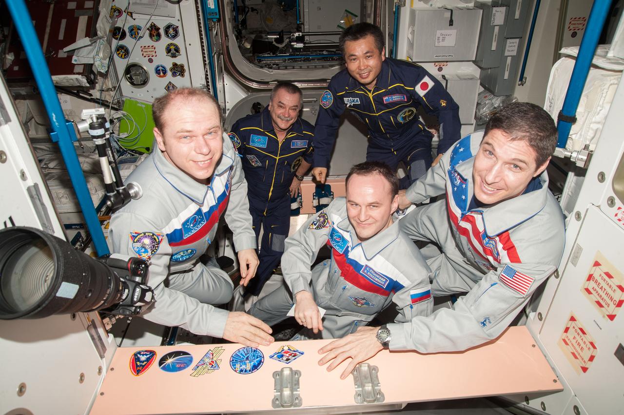 ISS038-E-066867 (9 March 2014) ---  In the Unity node onboard the Earth-orbiting International Space Station, three Expediton 38 crew members   affix their crew insignia just hours before departing the orbital complex.  From left to right, foreground, are cosmonauts Oleg Kotov and Sergey Ryazanskiy of Russia's Federal Space Agency (Roscosmos) and astronaut Mike Hopkins of NASA. Looking on in the background are cosmonaut Mikhail Tyurin of Roscosmos, Expedition 39 flight engineer, and Japan Aerospace Exploration Agency (JAXA) astronaut Koichi Wakata, Expedition 39 commander. Out of the frame is NASA astronaut Rick Mastracchio, Expedition 39 flight engineer.