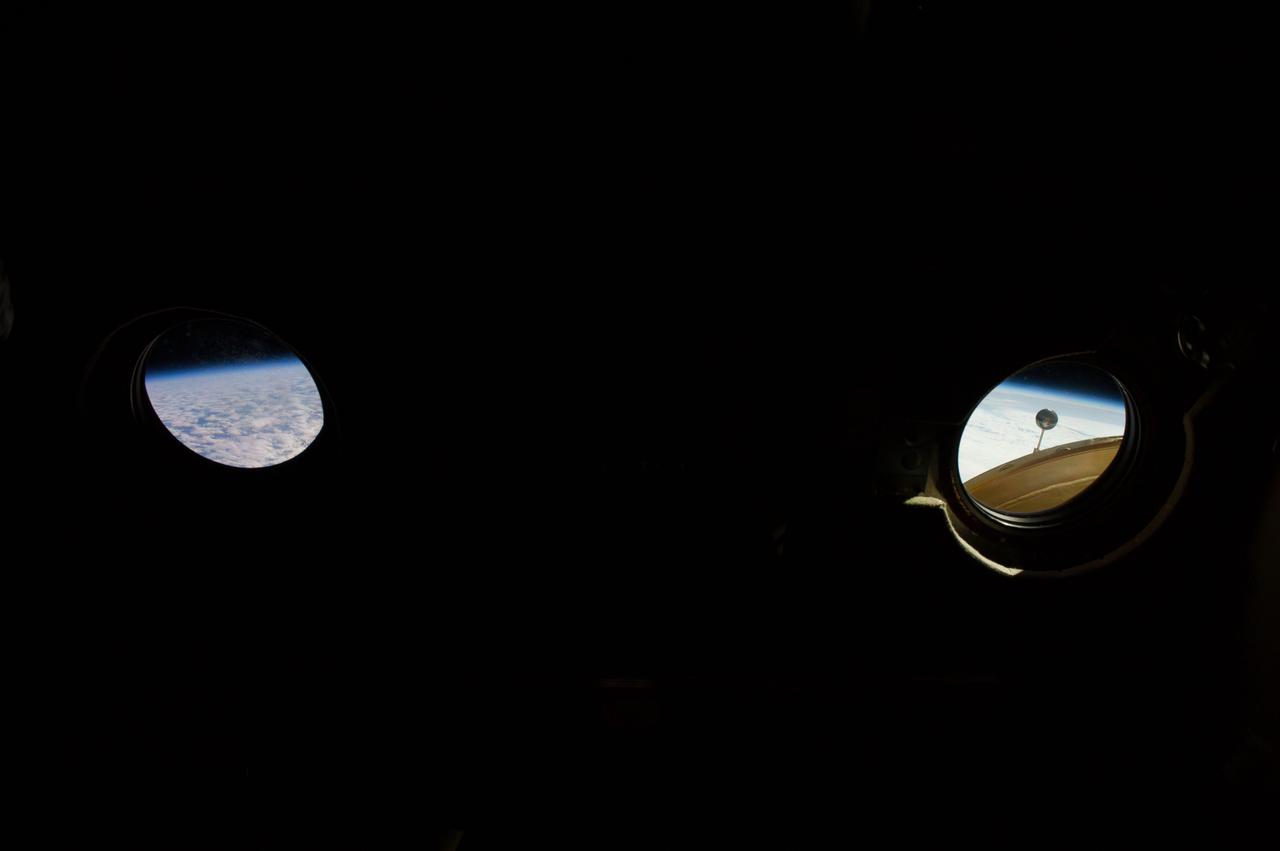 ISS039-E-000021 (11 March 2014)  --- With darkness in the Zvezda Service Module, the view outside two windows in the module photographed in the early hours of Expedition 39, an Earth horizon (left) and portions of the Pirs Docking Compartment are visible. In the right window, part of a Strela crane and part of an antenna,  both attached to the Pirs, can be seen.