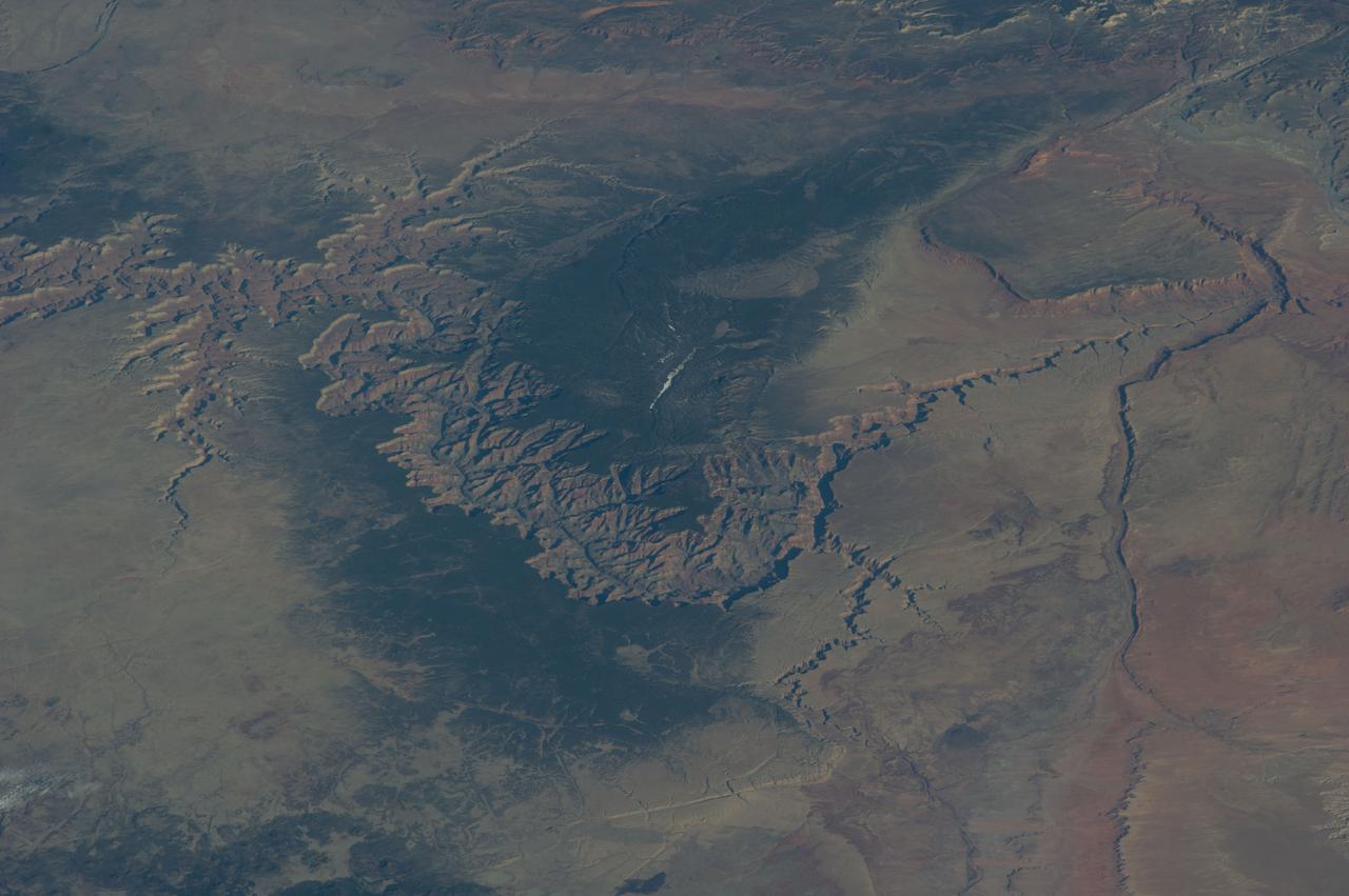 ISS039-E-005258 (25 March 2014) --- Not only do millions of tourists have special attractions to the Grand Canyon, but also through the years astronauts and cosmonauts in space. One of the Expedition 39 crew members aboard the Earth-orbiting International Space Station aimed his camera, equipped with a 180mm lens, at the iconic feature. The steep walls of the Colorado River canyon and its many side canyons make an intricate landscape that contrasts with the dark green, forested plateau to the north and south.  The Colorado River has done all the erosional work of carving away cubic kilometers of rock in a geologically short period of time.  Visible as a darker line snaking along the bottom of the canyon, the river lies at an altitude of 715 meters (2,345 feet), thousands of meters below the North and South Rims.  Temperatures are furnace-like on the river banks in the summer. But Grand Canyon Village, the classic outlook point for visitors, enjoys a milder climate at an altitude of 2,100 meters (6,890 feet).  The Grand Canyon has become a geologic icon?a place where, geologists say, one can almost sense the invisible tectonic forces within the Earth.  The North and South Rims are part of the Kaibab Plateau, a gentle tectonic swell in the landscape.  The uplift of the plateau had two pronounced effects on the landscape that show up in this image. First, in drier parts of the world, forests usually indicate higher places; higher altitudes are cooler and wetter, conditions that allow trees to grow.  The other geologic lesson on view is the canyon itself. Geologists now know that a river can cut a canyon only if the Earth surface rises vertically.  If such uplift is not rapid, a river can maintain its course by eroding huge quantities of rock and forming a canyon.