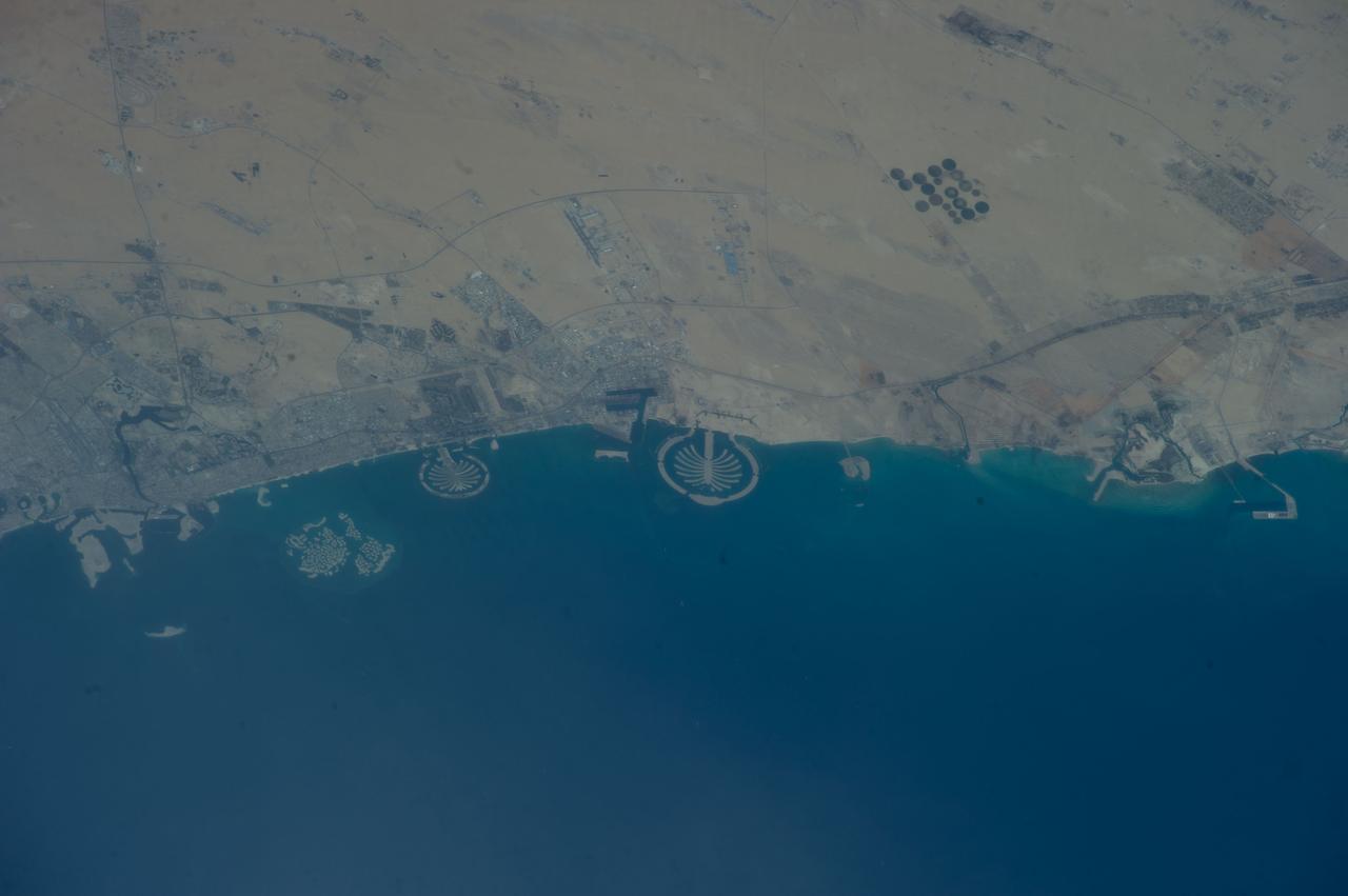ISS039-E-011515 (13 April 2014) --- Man-made archipelagos near Dubai, United Arab Emirates, are featured in this image photographed by an Expedition 39 crew member on the International Space Station, flying at 220 miles above Earth. The municipality of Dubai is the largest city of the Persian Gulf emirate of the same name, and has built a global reputation for large-scale developments and architectural works. Among the most visible of these developments -- particularly from the perspective of astronauts onboard the ISS -- are three man-made archipelagos. The two Palm Islands -- Palm Jumeirah to the left of center, and Palm Jebel Ali, just to the right of center, appear as stylized palm trees when viewed from above. The World Islands (near left edge) evoke a rough map of the world from an air- or space-borne perspective. The Palm Jumeirah project began in 2001 and required more than 50 million cubic meters of dredged sand to raise the islands above the Persian Gulf sea level. Construction of the Palm Jumeirah islands was completed in 2006; they are now being developed for residential and commercial housing and infrastructure. Creation of the World Islands was begun in 2003 and completed in 2008, using 320 million cubic meters of sand and 37 million tons of rock for the surrounding 27 kilometer-long protective breakwater.