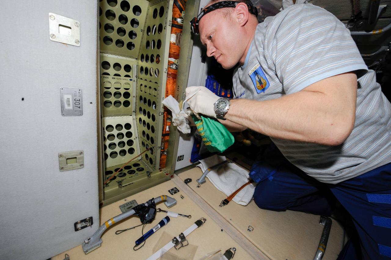 Expedition 39 flight engineer and Roscosmos cosmonaut Oleg Artemyev works to treat the area behind Panel 307 with a fungicide. Image was taken in the Zarya Functional Cargo Block (FGB).