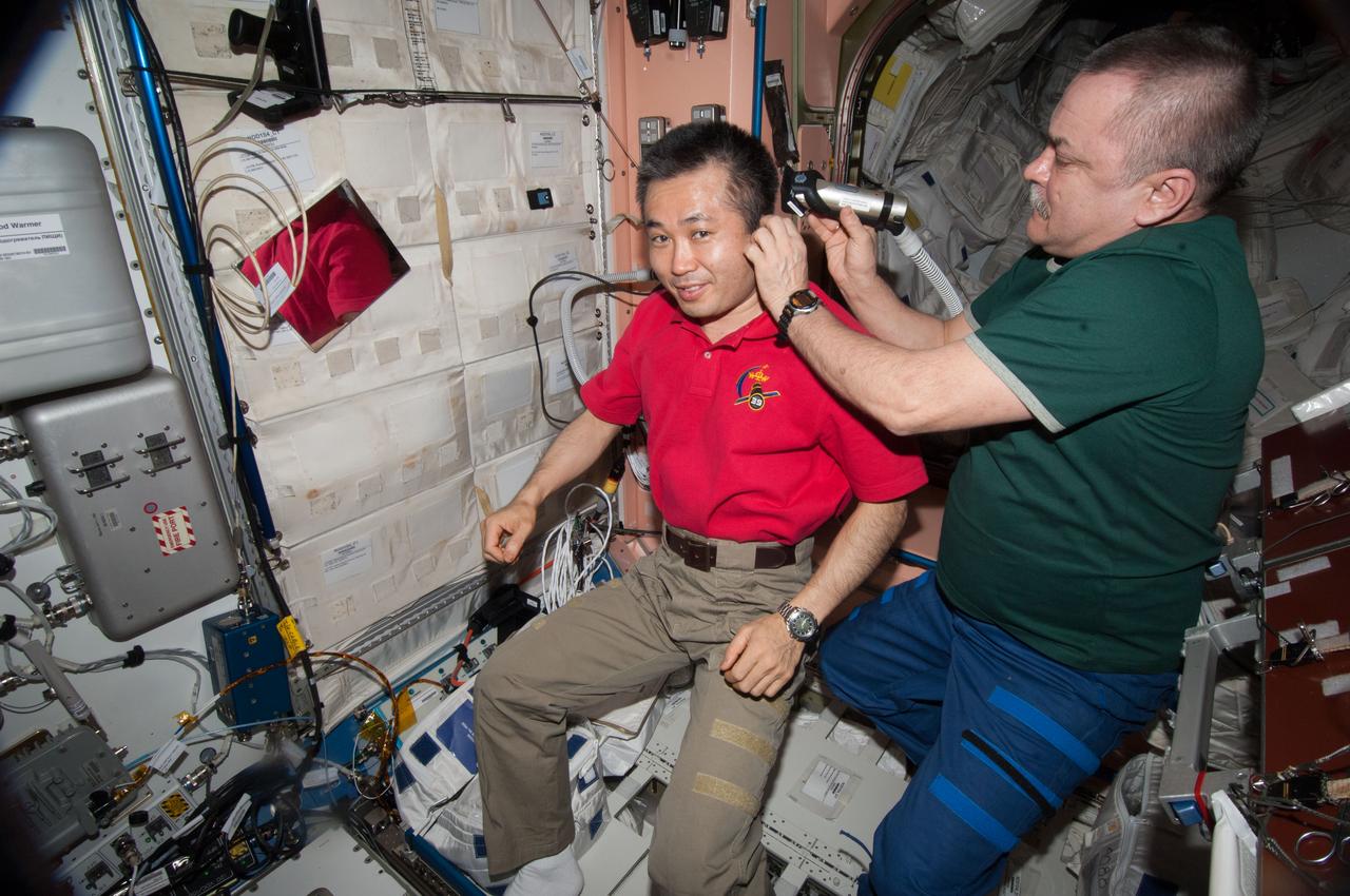 ISS039-E-015618 (26 April 2014) --- Expedition 39 Commander Koichi Wakata of the Japan Aerospace Exploration Agency (JAXA) sits motionless while Flight Engineer Mikhail Tyurin of Russia's Federal Space Agency (Roscosmos) cuts his hair in the Unity node of the Earth-orbiting International Space Station.