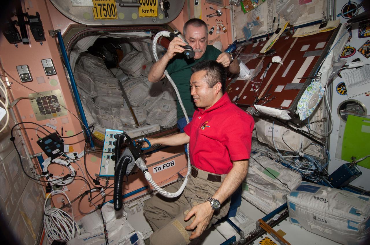 ISS039-E-015627 (26 April 2014) --- Expedition 39 Commander Koichi Wakata of the Japan Aerospace Exploration Agency (JAXA) sits motionless while Flight Engineer Mikhail Tyurin of Russia's Federal Space Agency (Roscosmos) cuts his hair in the Unity node of the Earth-orbiting International Space Station.
