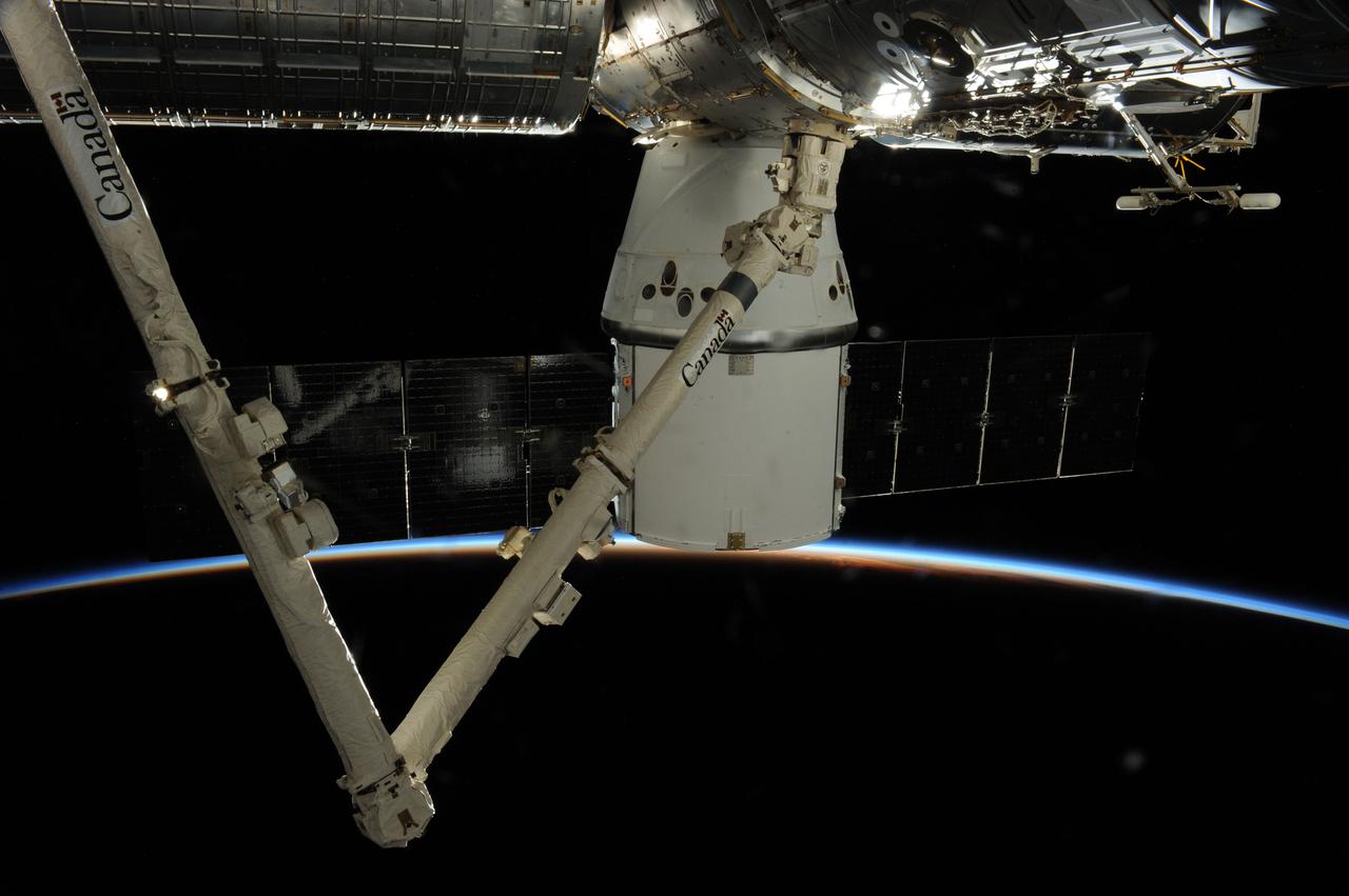 ISS039-E-017064 (26 April 2014) --- One of the Expedition 39 crew members, positioned in the Cupola of the International Space Station, photographed this view of the SpaceX Dragon berthed to the orbital outpost for several days. A thin sliver of Earth's atmosphere runs through the center of the scene. The Space Station Remote Manipulator System (SSRMS) arm or Canadarm 2 is in the left side of the frame.