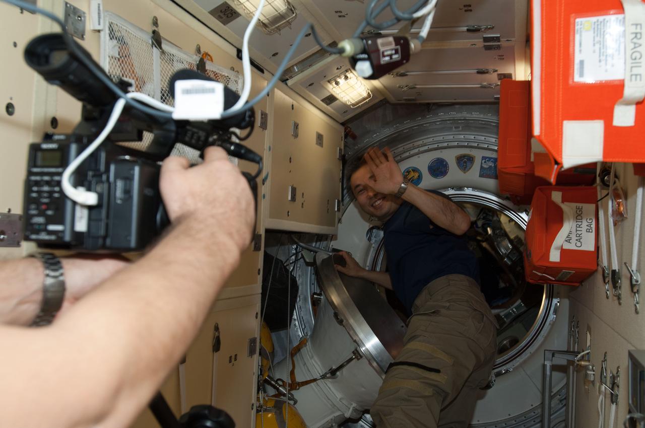 ISS039-E-020769 (13 May 2013) --- Expedition 39 Commander Koichi Wakata of the Japan Aerospace Exploration Agency waves good bye as one of the three remaining crew members on the orbital outpost records video of the crew departure. Already on the other side of the hatch are Expedition Flight Engineers Rick Mastracchio of NASA and Mikhail Tyurin of Russia's Federal Space Agency (Roscosmos).