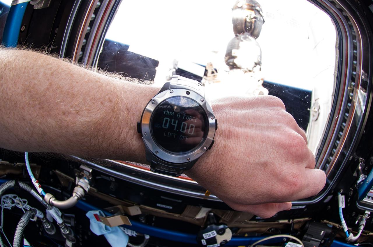 View of docked Soyuz 39 (TMA-13M) on Mini-Research Module 1 (MRM1) (Rassvet). A wrist watch is visible in the frame with the terms "Max 6 Force 04:00" on its face.