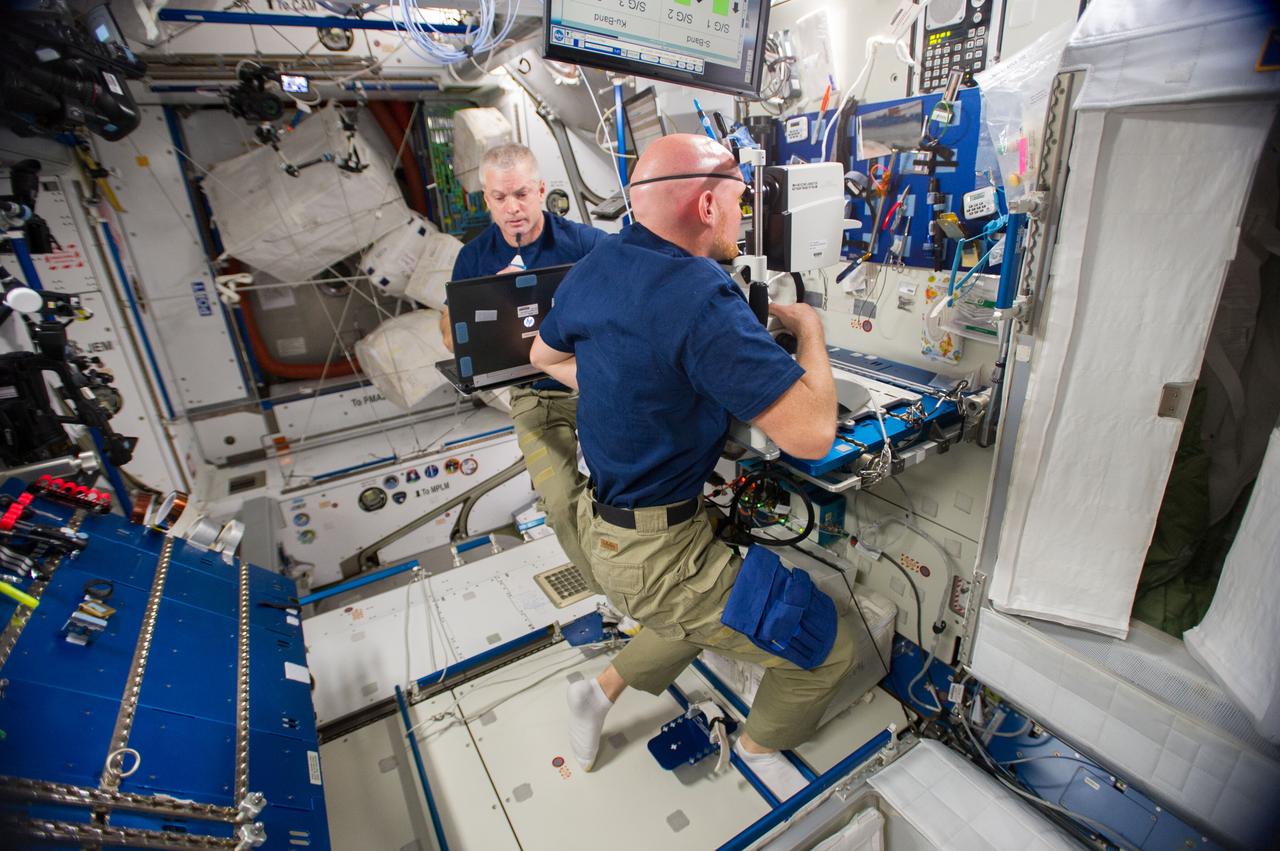 ISS040-E-006739 (3 June 2014) --- European Space Agency astronaut Alexander Gerst, Expedition 40 flight engineer, uses the Optical Coherence Tomography (OCT) camera during an Ocular Health (OH) vision test in the Harmony node of the International Space Station. The OH experiment observes and seeks to understand vision changes during long-term space missions. NASA astronaut Steve Swanson (left), Expedition 40 commander, assists Gerst.