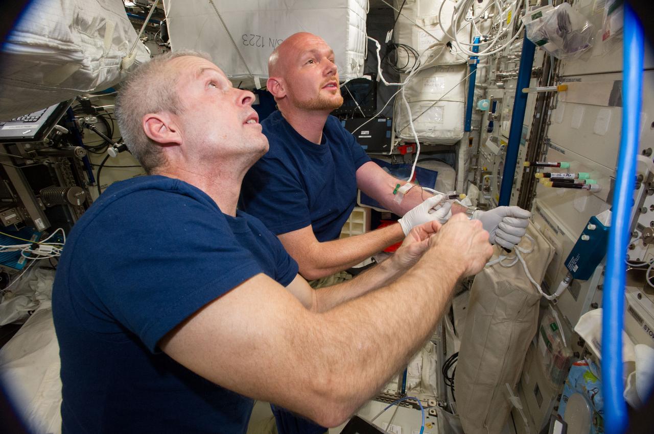 Astronaut Alexander Gerst,Expedition 40 flight engineer (background),and Expedition 40 Commander Steve Swanson are photographed performing blood sample collection in the Columbus module as part of HRF Generic Frozen Blood Collection Operations.