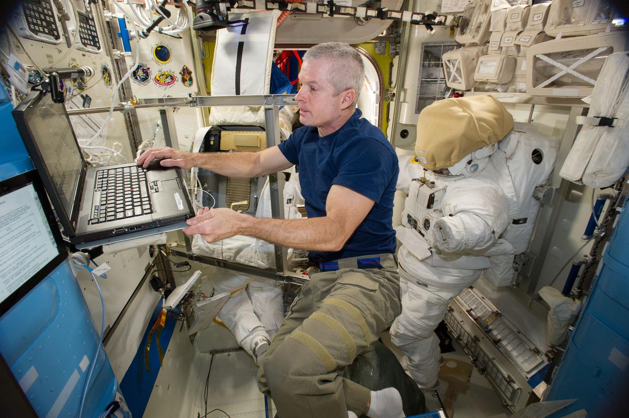 ISS040-E-007682 (5 June 2014) --- NASA astronaut Reid Wiseman, Expedition 40 flight engineer, uses a computer while working with an Extravehicular Mobility Unit (EMU) spacesuit in the Quest airlock of the International Space Station.