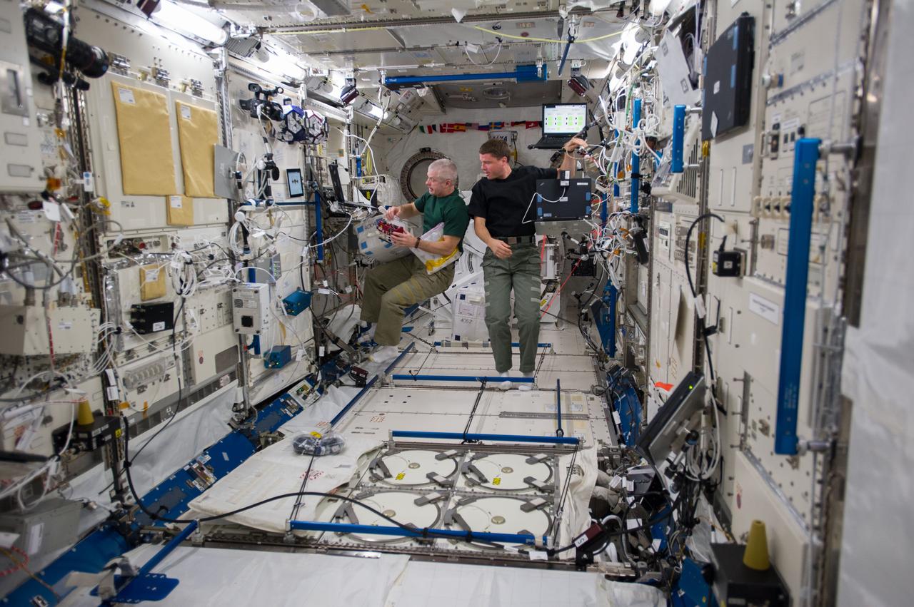 ISS040-E-013914 (18 June 2014) --- In the International Space Station's Kibo laboratory, NASA astronauts Steve Swanson (left), Expedition 40 commander; and Reid Wiseman, flight engineer, conduct test runs of the SPHERES-Slosh experiment, using the soccer-ball-sized, free-flying satellites known as Synchronized Position Hold, Engage, Reorient, Experimental Satellites, or SPHERES. The SPHERES-Slosh investigation uses small robotic satellites on the space station to examine how liquids move around inside containers in microgravity.