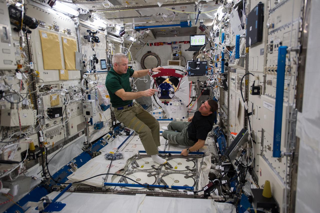 ISS040-E-014444 (18 June 2014) --- In the International Space Station's Kibo laboratory, NASA astronauts Steve Swanson (left), Expedition 40 commander; and Reid Wiseman, flight engineer, conduct test runs of the SPHERES-Slosh experiment, using the soccer-ball-sized, free-flying satellites known as Synchronized Position Hold, Engage, Reorient, Experimental Satellites, or SPHERES. The SPHERES-Slosh investigation uses small robotic satellites on the space station to examine how liquids move around inside containers in microgravity.