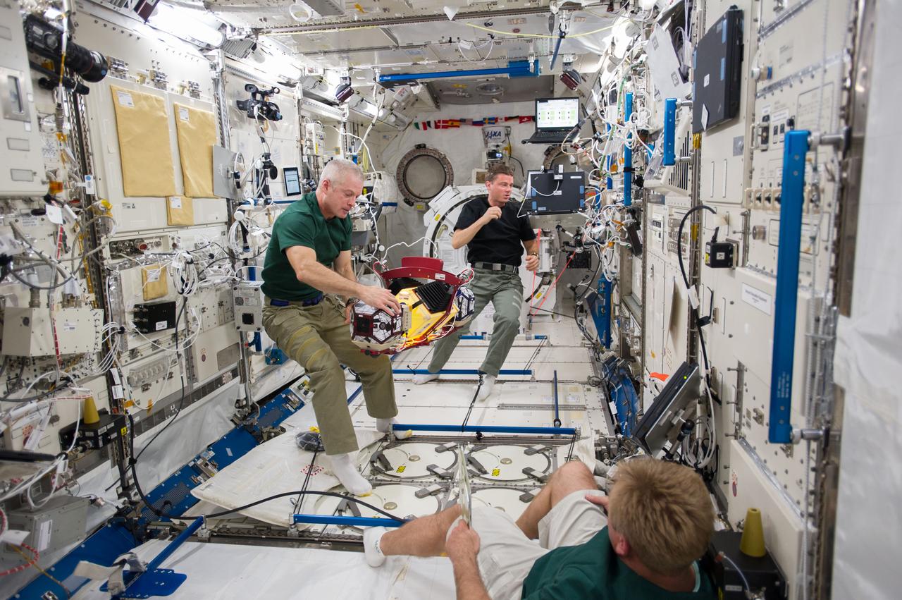 ISS040-E-014468 (18 June 2014) --- In the International Space Station's Kibo laboratory, NASA astronauts Steve Swanson (left), Expedition 40 commander; and Reid Wiseman, flight engineer, conduct test runs of the SPHERES-Slosh experiment, using the soccer-ball-sized, free-flying satellites known as Synchronized Position Hold, Engage, Reorient, Experimental Satellites, or SPHERES. The SPHERES-Slosh investigation uses small robotic satellites on the space station to examine how liquids move around inside containers in microgravity. Russian cosmonaut Maxim Suraev (bottom right), flight engineer, looks on.