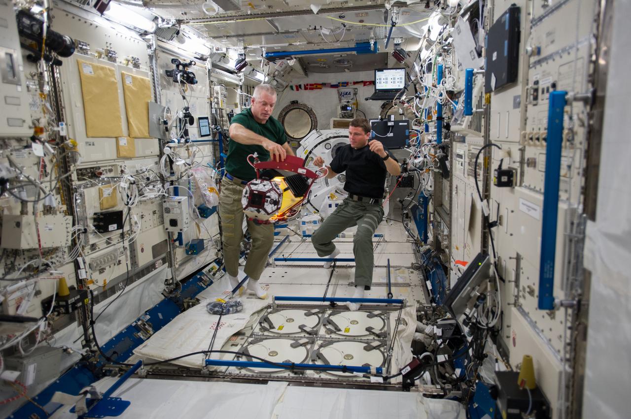 ISS040-E-014536 (18 June 2014) --- In the International Space Station's Kibo laboratory, NASA astronauts Steve Swanson (left), Expedition 40 commander; and Reid Wiseman, flight engineer, conduct test runs of the SPHERES-Slosh experiment, using the soccer-ball-sized, free-flying satellites known as Synchronized Position Hold, Engage, Reorient, Experimental Satellites, or SPHERES. The SPHERES-Slosh investigation uses small robotic satellites on the space station to examine how liquids move around inside containers in microgravity.