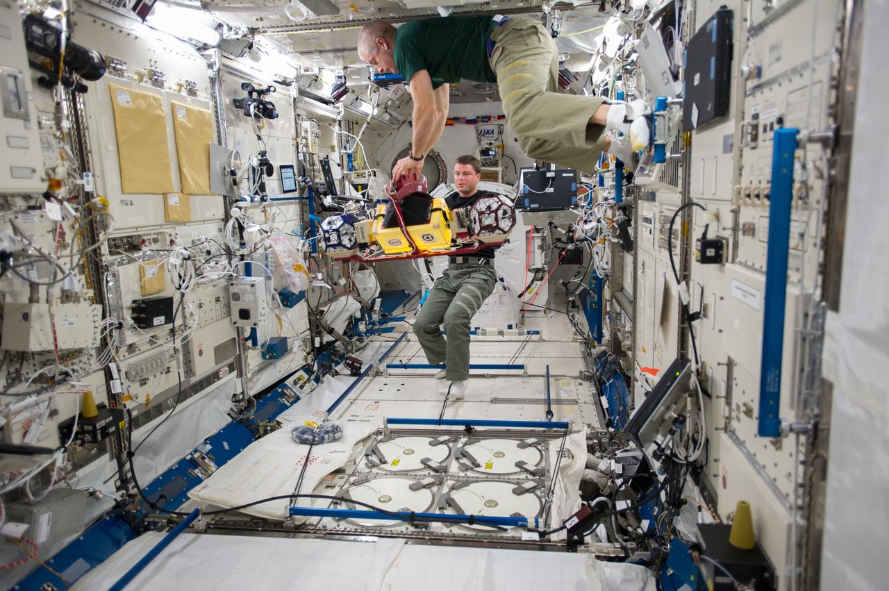 ISS040-E-014615 (18 June 2014) --- In the International Space Station's Kibo laboratory, NASA astronauts Steve Swanson (top), Expedition 40 commander; and Reid Wiseman, flight engineer, conduct test runs of the SPHERES-Slosh experiment, using the soccer-ball-sized, free-flying satellites known as Synchronized Position Hold, Engage, Reorient, Experimental Satellites, or SPHERES. The SPHERES-Slosh investigation uses small robotic satellites on the space station to examine how liquids move around inside containers in microgravity.