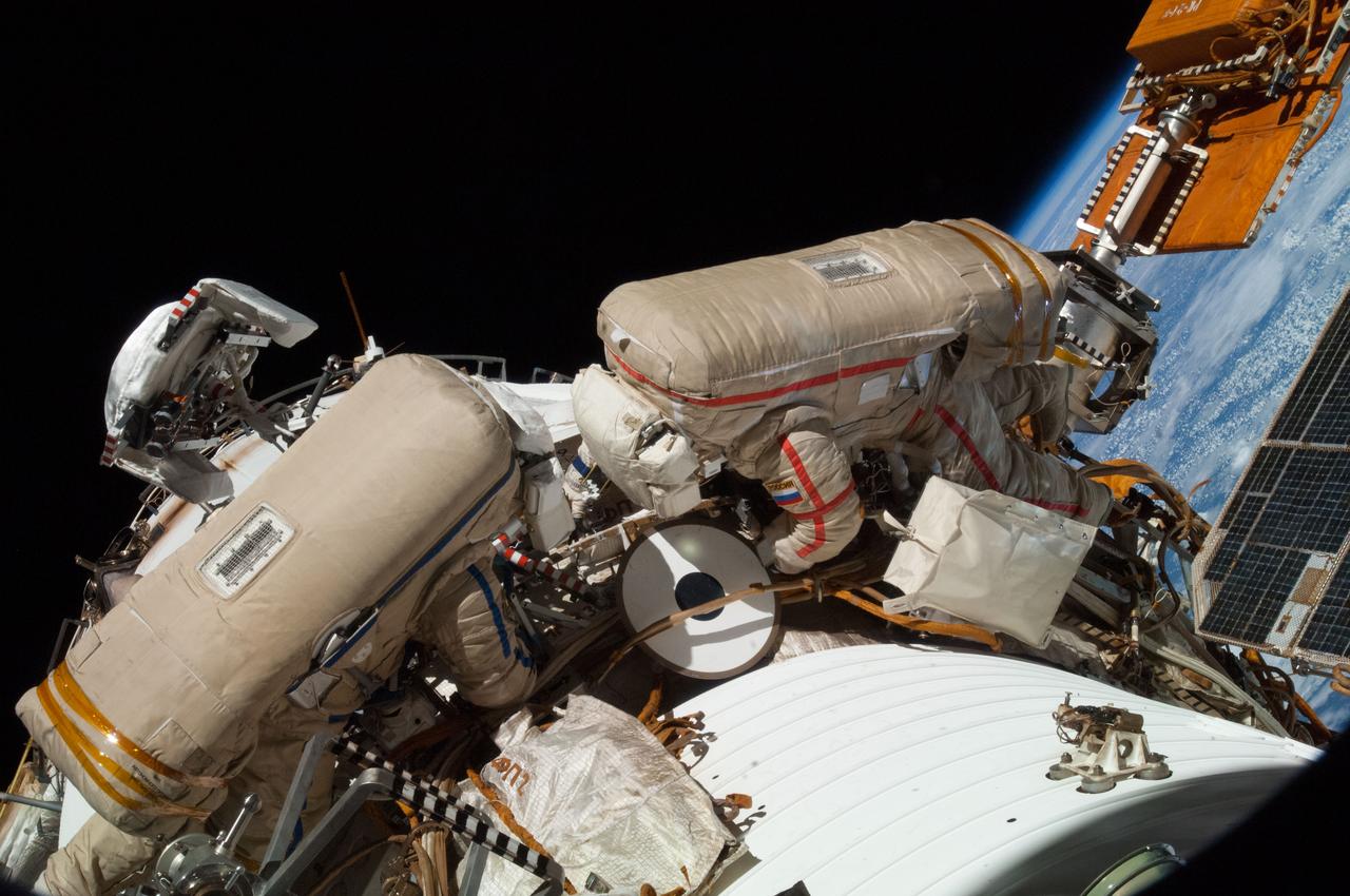 Cosmonaut Oleg Artemyev (EV2),in the blue striped Orlan suit,and Cosmonaut Alexander Skvortsov,in the red striped Orlan suit,are photographed at work during Russian EVA 38 by Expedition 40 crewmembers aboard the ISS. They are working to Installed the AFAR (Automatic Phased Array Antenna) Unit of the [EKTC] (Integrated Command and Telemetry System) external FU (Feeder Unit) between PI.II-III on Service Module (SM) circumferential handrails.