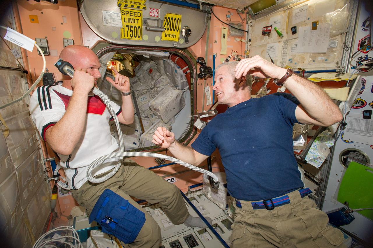 ISS040-E-020361 (26 June 2014) --- NASA astronaut Steve Swanson (right), Expedition 40 commander; and European Space Agency astronaut Alexander Gerst, flight engineer, enjoy a light moment in the Unity node of the International Space Station. Gerst is holding hair clippers fashioned with a vacuum device to garner freshly cut hair. A friendly World Cup Soccer-related agreement between the crew members representing the USA, and Gerst, a German citizen who represents the European Space Agency, called for the American losers of a German-USA match to have their heads shaved. The German team won the match 1-0.