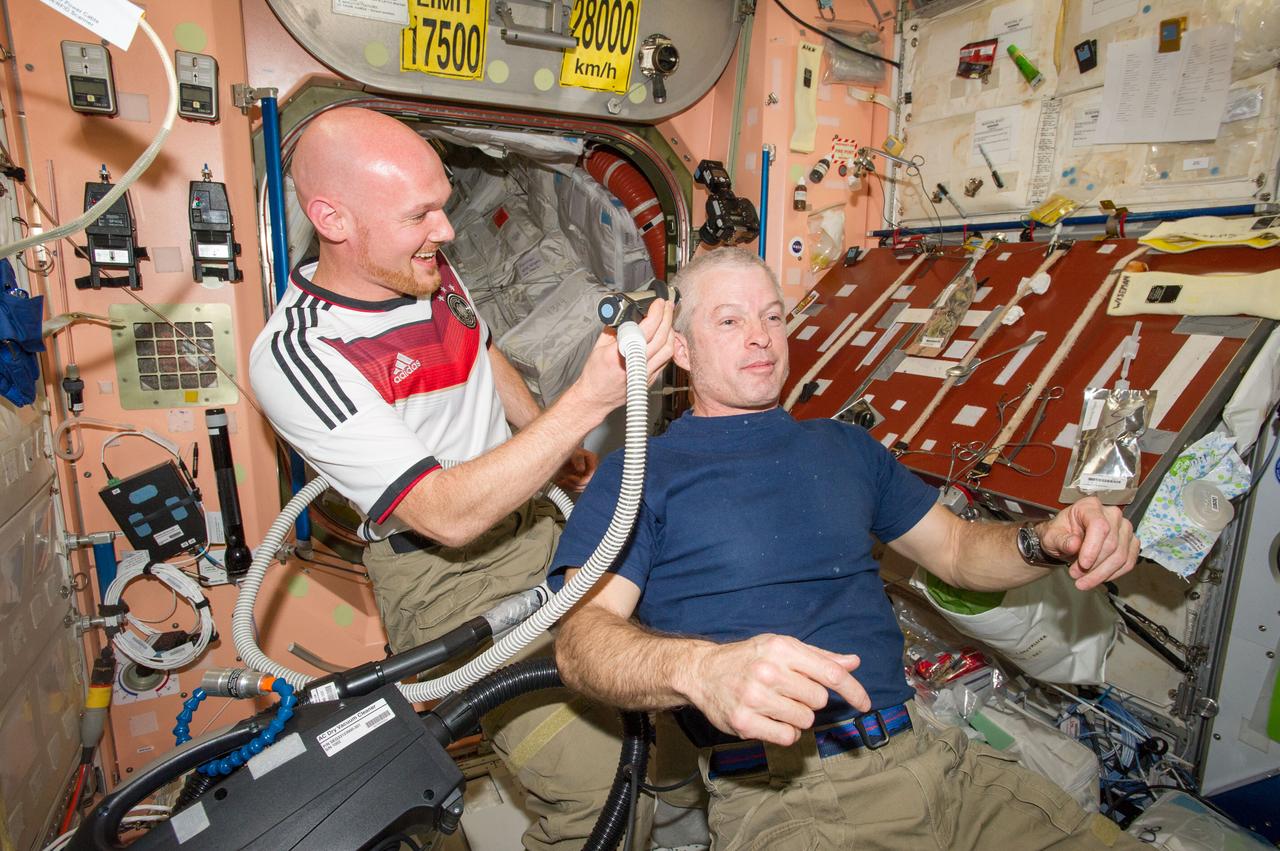 ISS040-E-020364 (26 June 2014) --- European Space Agency astronaut Alexander Gerst, Expedition 40 flight engineer, shaves the head of NASA astronaut Steve Swanson, commander, in the Unity node of the International Space Station. Gerst used hair clippers fashioned with a vacuum device to garner freshly cut hair. A friendly World Cup Soccer-related agreement between the crew members representing the USA, and Gerst, a German citizen who represents the European Space Agency, called for the American losers of a German-USA match to have their heads shaved. The German team won the match 1-0.