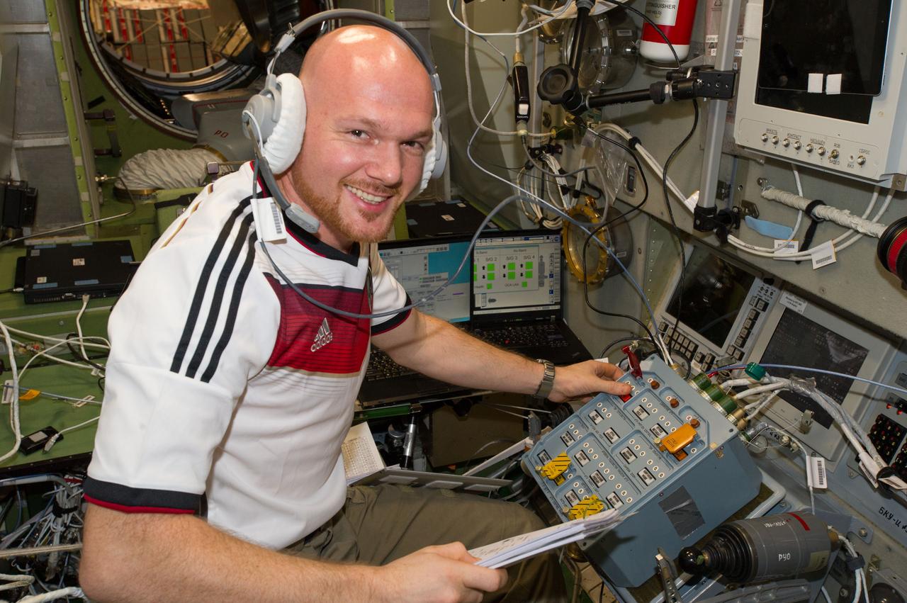 ESA astronaut Alexander Gerst, Expedition 40 flight engineer (wearing soccer shirt), is photographed during ATV equipment preparation in the Service Module (SM) prior to ATV launch.