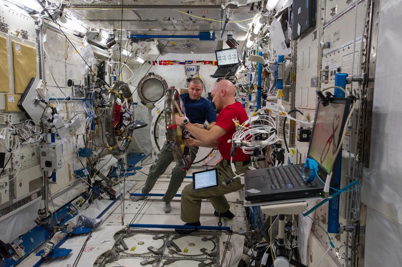 ISS040-E-059344 (10 July 2014) --- In the International Space Station’s Kibo laboratory, NASA astronaut Reid Wiseman (left) and European Space Agency astronaut Alexander Gerst, both Expedition 40 flight engineers, conduct a session with a pair of bowling-ball-sized free-flying satellites known as Synchronized Position Hold, Engage, Reorient, Experimental Satellites, or SPHERES. Surrounding the two SPHERES mini-satellites is ring-shaped hardware known as the Resonant Inductive Near-field Generation System, or RINGS. SPHERES-RINGS seeks to demonstrate wireless power transfer between satellites at a distance for enhanced operations.