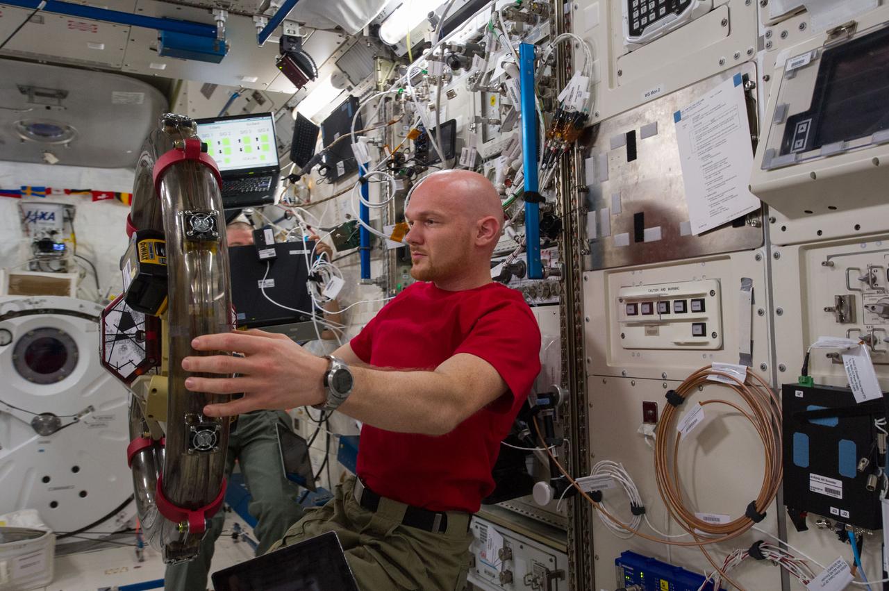 ISS040-E-059467 (10 July 2014) --- In the International Space Station's Kibo laboratory, European Space Agency astronaut Alexander Gerst and NASA astronaut Reid Wiseman (mostly obscured), both Expedition 40 flight engineers, conduct a session with a pair of bowling-ball-sized free-flying satellites known as Synchronized Position Hold, Engage, Reorient, Experimental Satellites, or SPHERES. Surrounding the two SPHERES mini-satellites is ring-shaped hardware known as the Resonant Inductive Near-field Generation System, or RINGS. SPHERES-RINGS seeks to demonstrate wireless power transfer between satellites at a distance for enhanced operations.