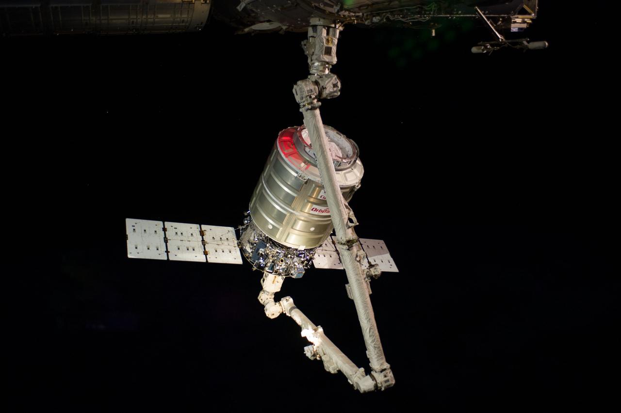 ISS040-E-067885 (16 July 2014) --- The Orbital Sciences’ Cygnus cargo craft attached to the end of the Canadarm2 robotic arm of the International Space Station is photographed by an Expedition 40 crew member after the two spacecraft converged at 6:36 a.m. (EDT) on July 16, 2014. The red color on Cygnus is a spectral effect from one of Cygnus’ strobe lights against the fading light heading into an orbital sunset following grapple.