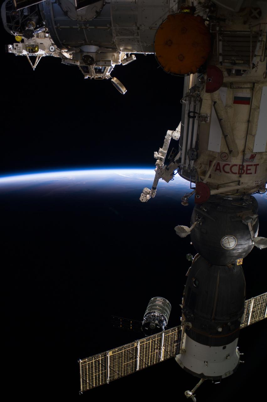 ISS040-E-068644 (16 July 2014) --- The Orbital Sciences? Cygnus cargo craft (bottom center) is photographed by an Expedition 40 crew member on the International Space Station during rendezvous and capture operations. The two spacecraft converged at 6:36 a.m. (EDT) on July 16, 2014. Also visible in this image are the station?s Cupola and the Tranquility node (top) and Canadarm2 (center) along with a Russian Soyuz spacecraft docked to the station. Earth?s horizon and the blackness of space provide the backdrop for the scene.