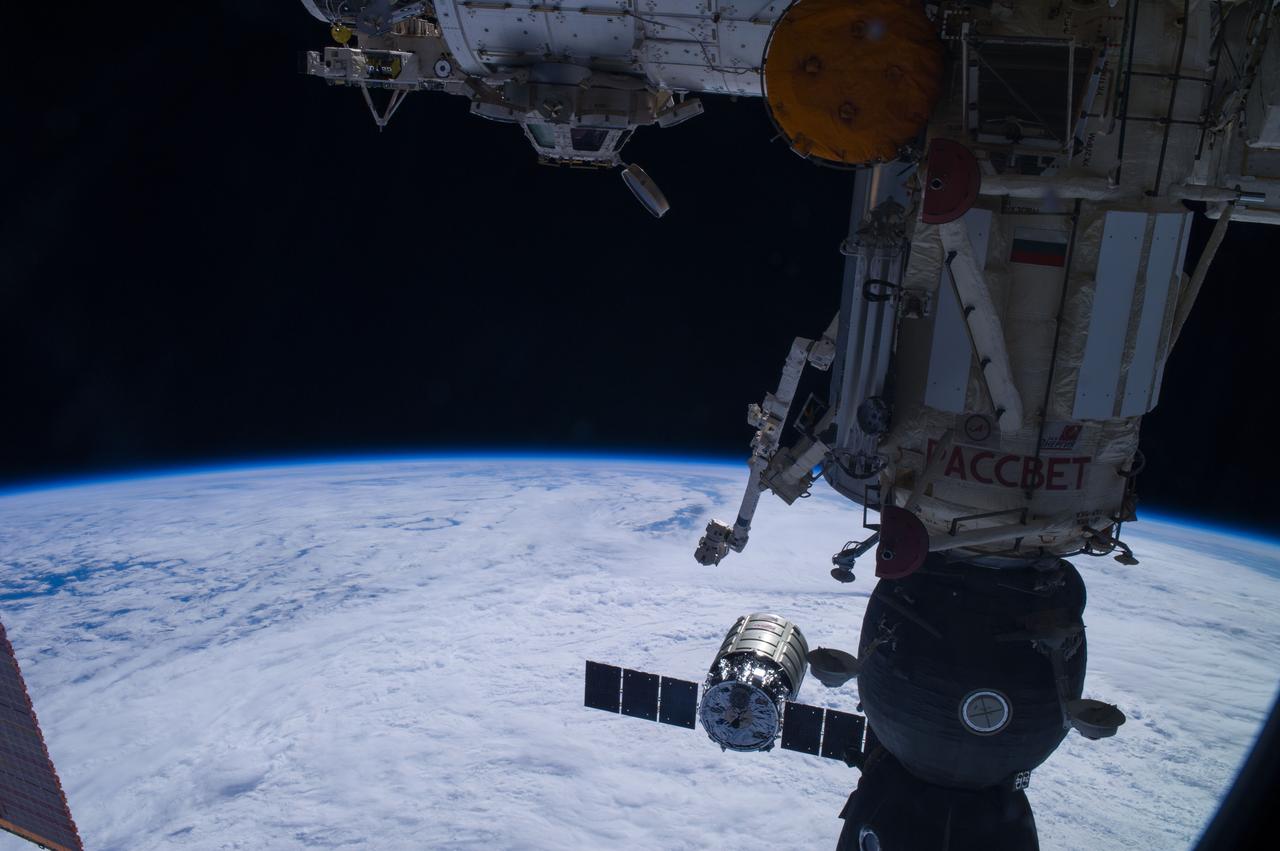 ISS040-E-068656 (16 July 2014) --- The Orbital Sciences? Cygnus cargo craft (bottom center) is photographed by an Expedition 40 crew member on the International Space Station during rendezvous and capture operations. The two spacecraft converged at 6:36 a.m. (EDT) on July 16, 2014. Also visible in this image are the station?s Cupola and the Tranquility node (top) and Canadarm2 (center) along with a Russian Soyuz spacecraft docked to the station. A cloud-covered part of Earth provides the backdrop for the scene.