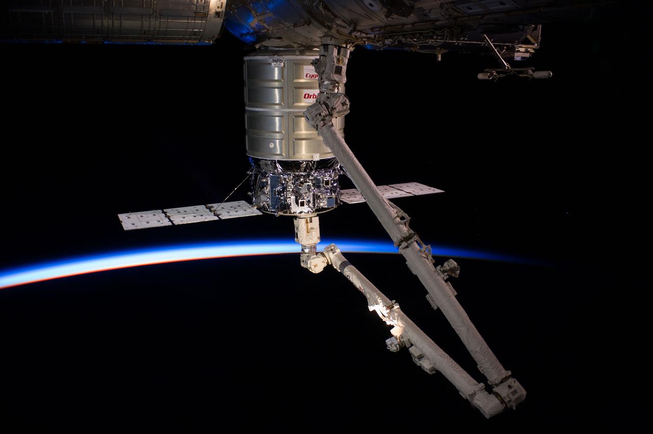 ISS040-E-069182 (16 July 2014) --- Intersecting the thin line of Earth’s atmosphere, the Orbital Sciences’ Cygnus cargo craft attached to the end of the Canadarm2 robotic arm is berthed to the nadir port of the Harmony node of the International Space Station.