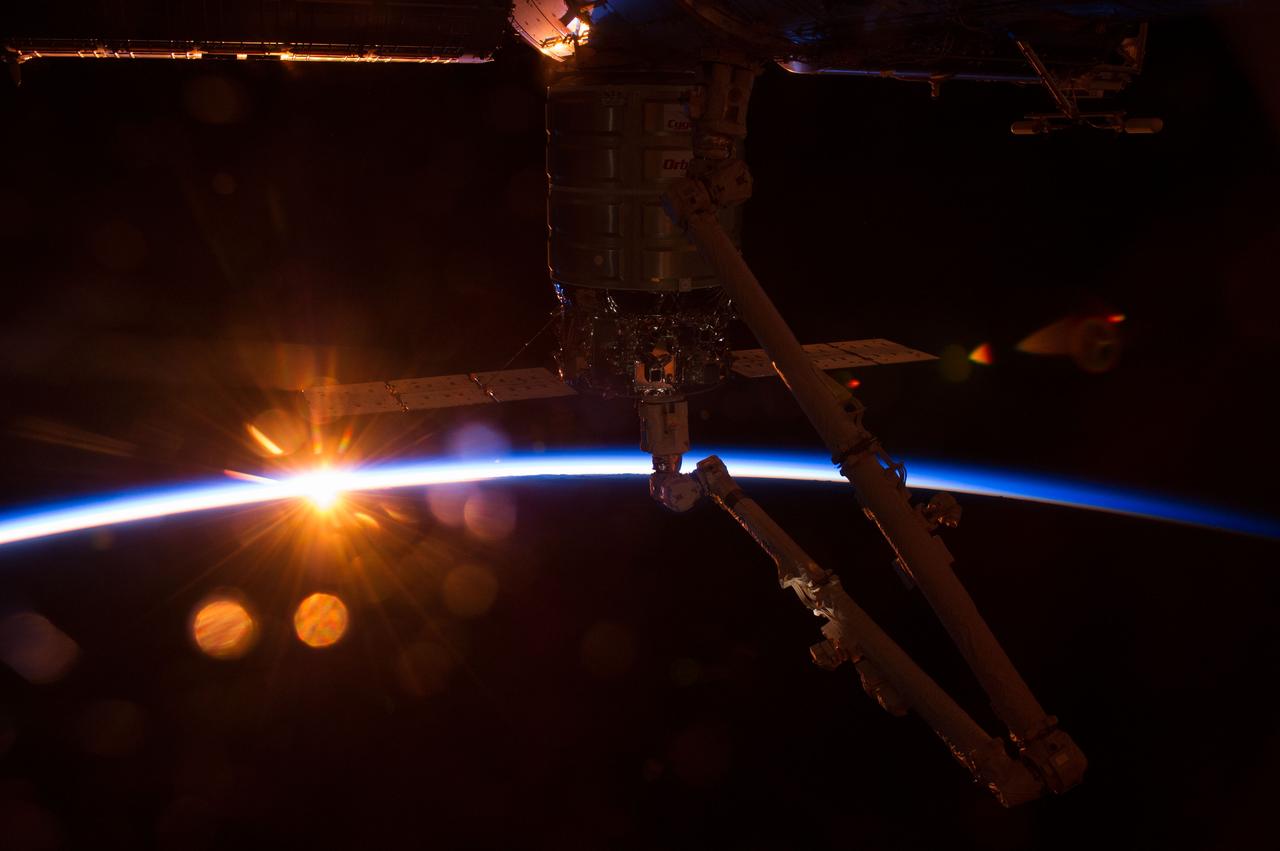 ISS040-E-069192 (16 July 2014) --- Intersecting the thin line of Earth’s atmosphere during an orbital sunrise, the Orbital Sciences’ Cygnus cargo craft attached to the end of the Canadarm2 robotic arm is berthed to the nadir port of the Harmony node of the International Space Station.
