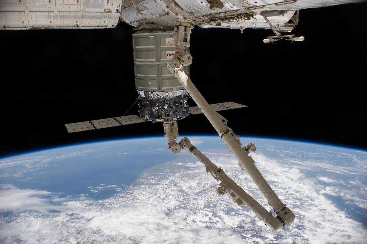 ISS040-E-069582 (16 July 2014) --- The Orbital Sciences’ Cygnus cargo craft attached to the end of the Canadarm2 robotic arm is berthed to the nadir port of the Harmony node of the International Space Station, photographed by an Expedition 40 crew member. A blue and white part of the Earth and the blackness of space provide the backdrop for the scene.